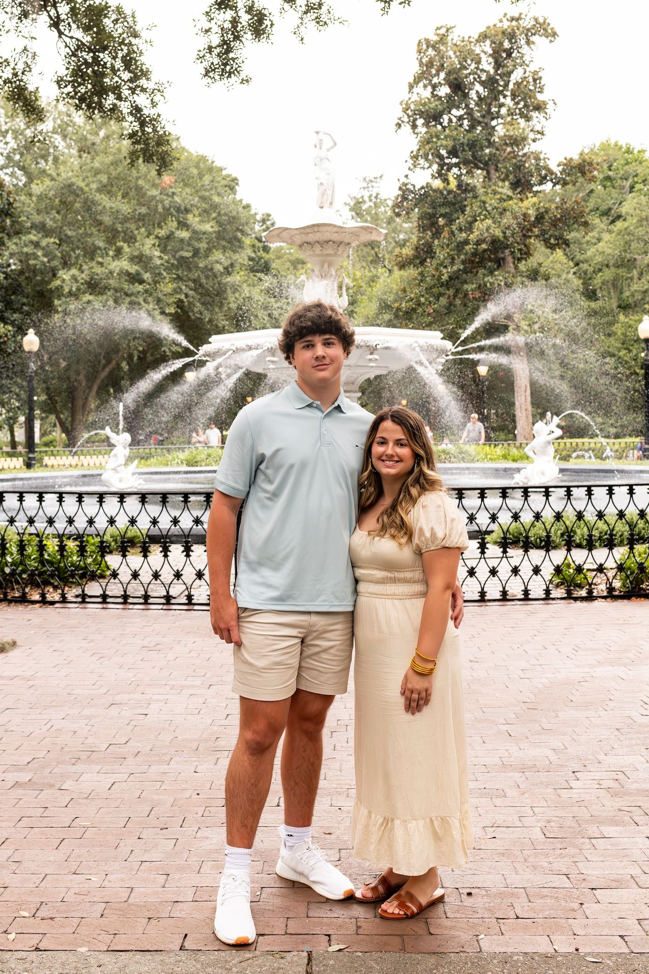 Couple in coordinated casual outfits standing in front of ornate water fountain display.