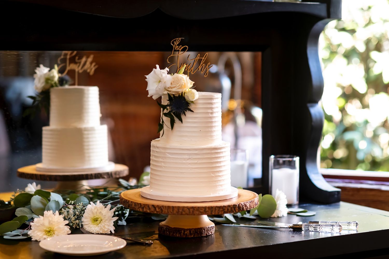 Two elegant white tiered wedding cakes with horizontal ribbing texture and floral decorations displayed on wooden cake stands.