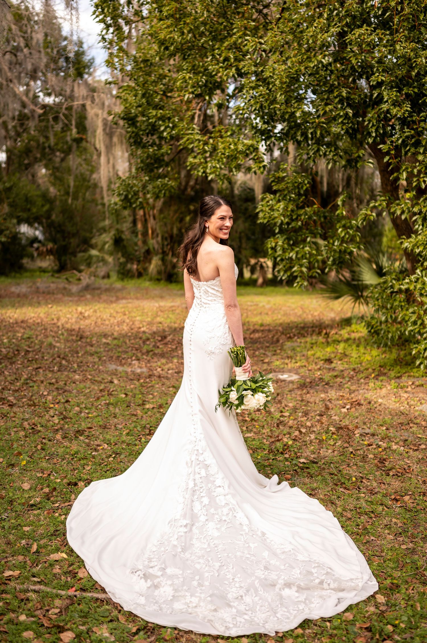 Elegant white lace mermaid wedding gown with long train photographed in outdoor garden setting with Spanish moss.