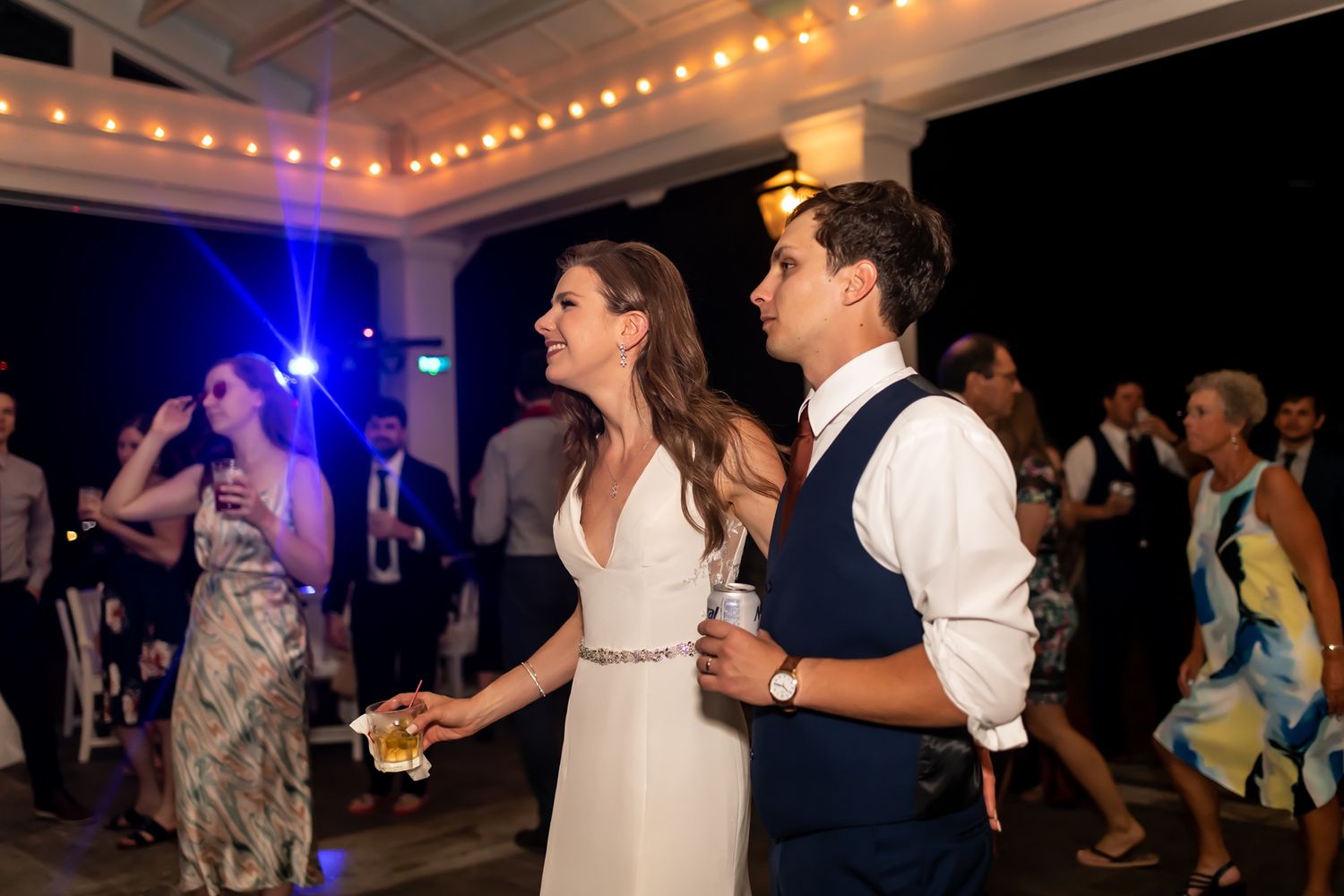Wedding guests dancing energetically on a dark dance floor illuminated by colorful lights at a nighttime reception.