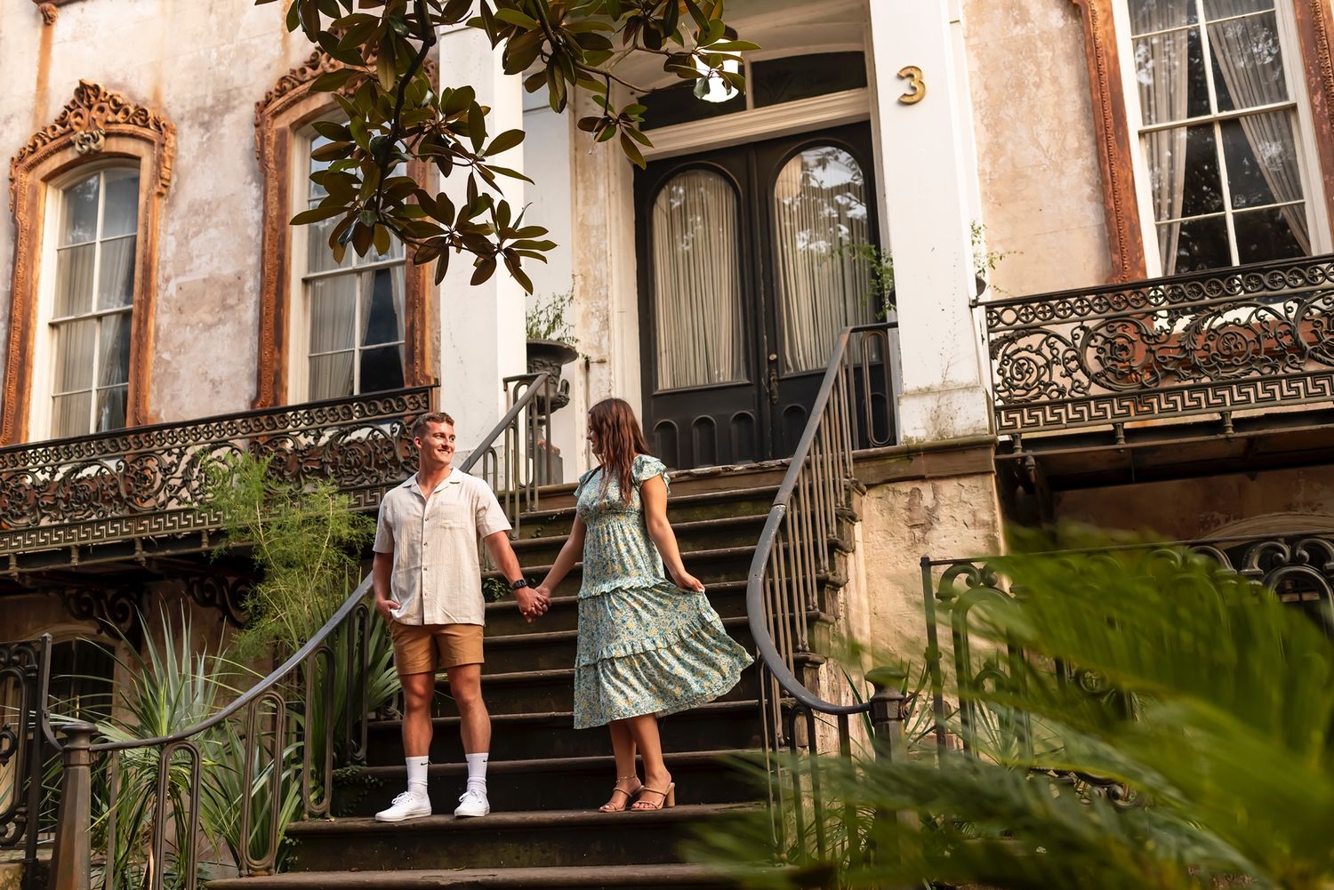 Two people descending ornate steps of a historic building with wrought iron railings in Savannah's historic district.