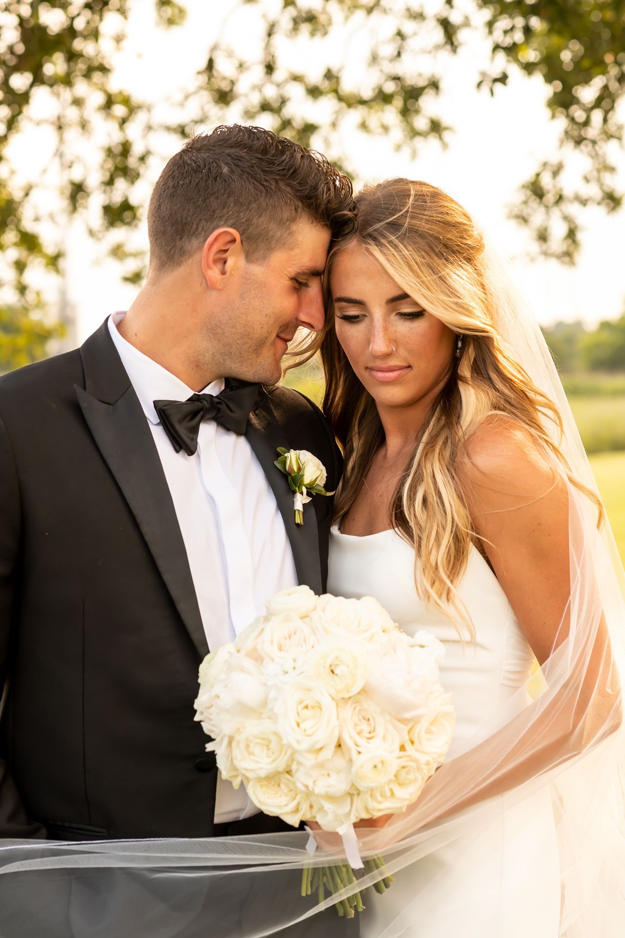 Romantic wedding portraits of a couple embracing on a bright sunlit day with white roses and a flowing veil.