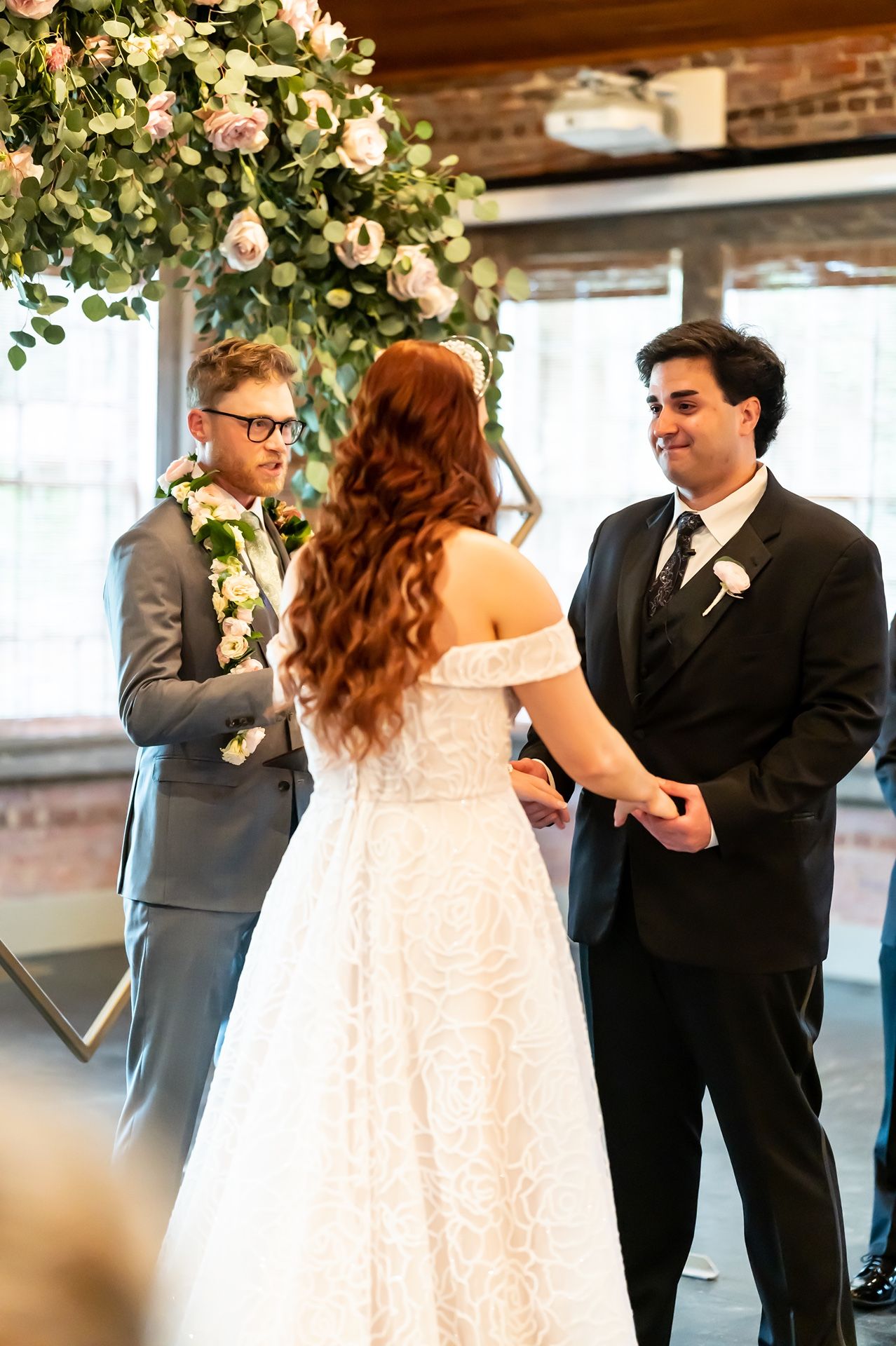 A couple shares a tender dance at their wedding reception surrounded by floral decorations and exposed brick walls.