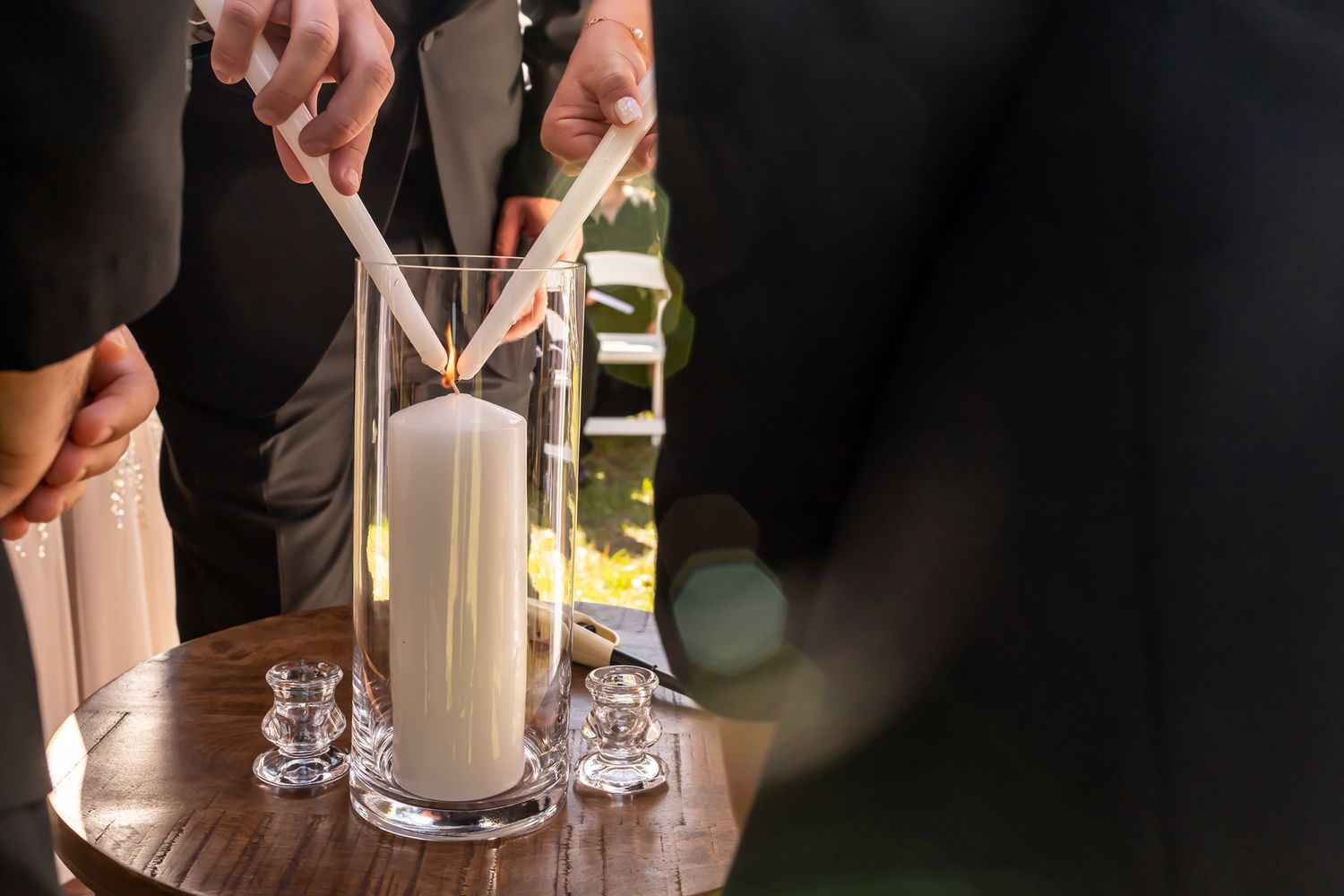 Multiple people pour champagne into tall glasses creating a cascading tower at an elegant celebration.