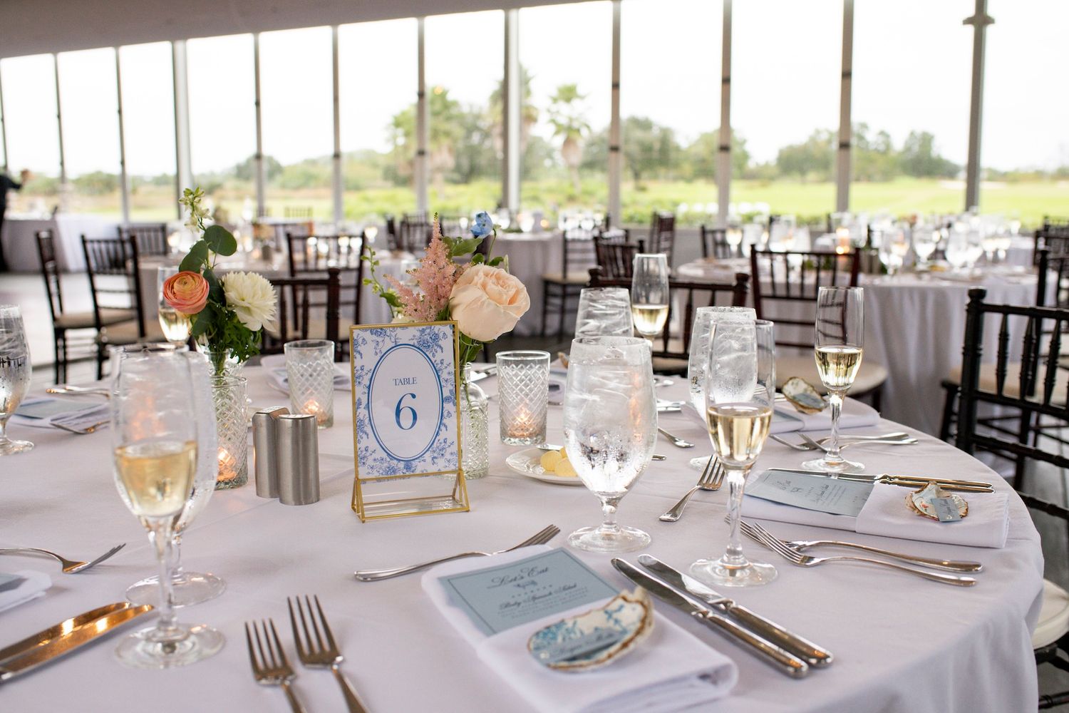 Elegant wedding reception table set with white linens, floral centerpiece, candles, wine glasses, and a table number 6 card.