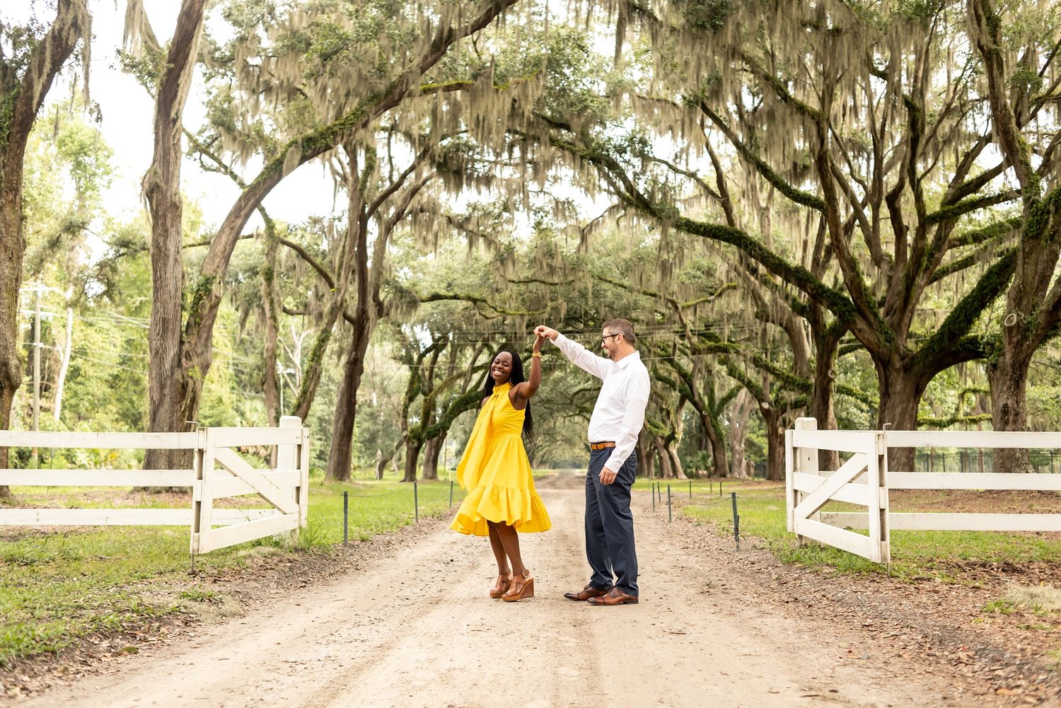 A dirt path winds through a lush garden setting with Spanish moss hanging from oak trees creating a romantic atmosphere.