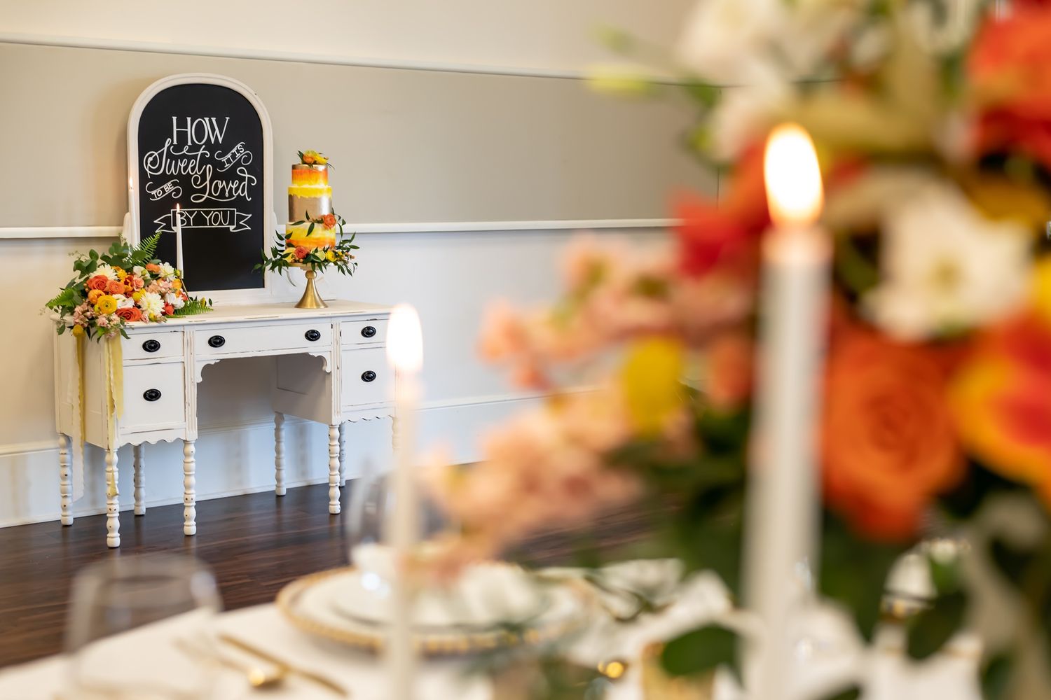 A white vintage vanity table decorated with fall flowers and chalkboard sign in a romantic wedding setting.