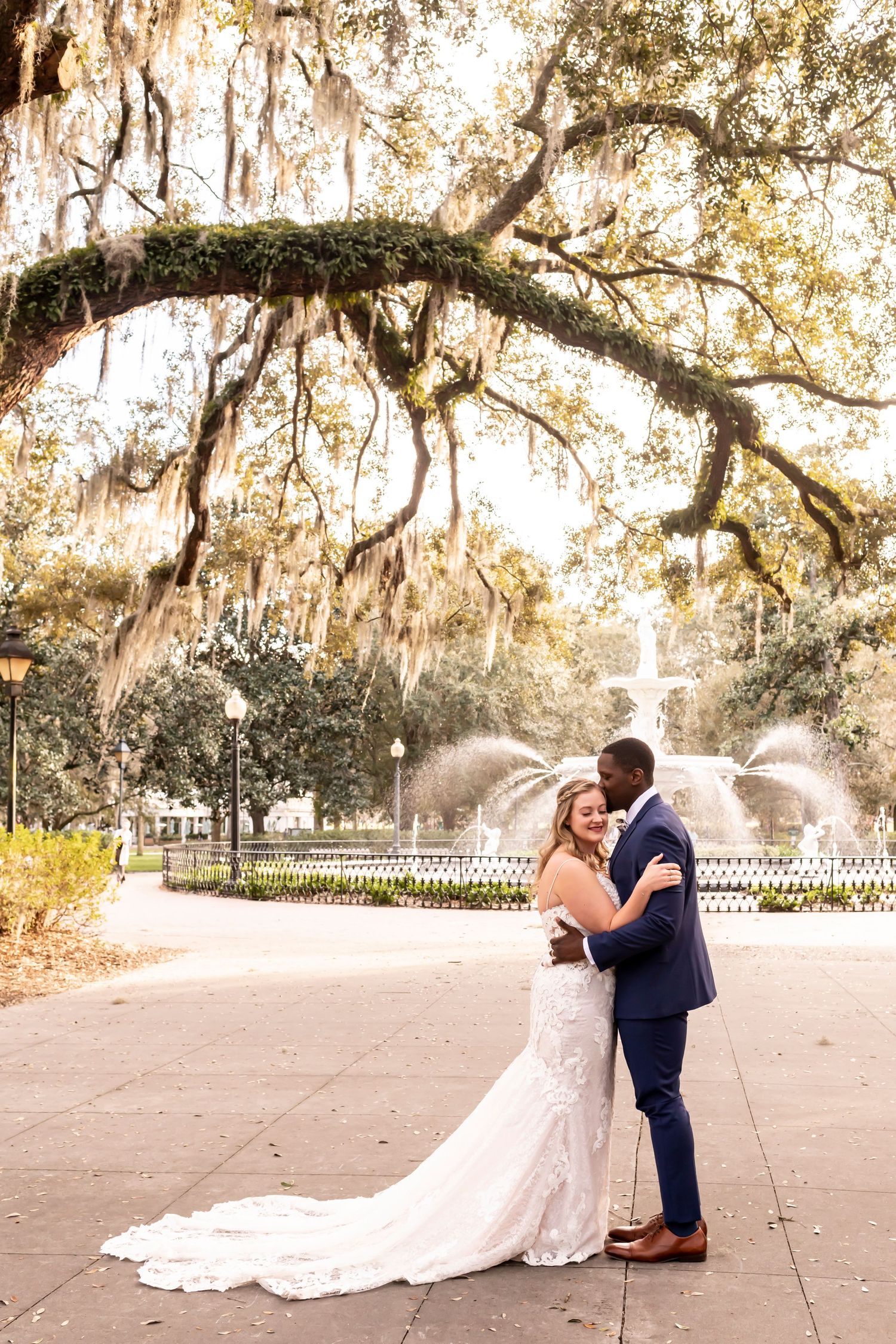 A romantic wedding couple embraces under Spanish moss covered oak trees in a beautiful garden setting.