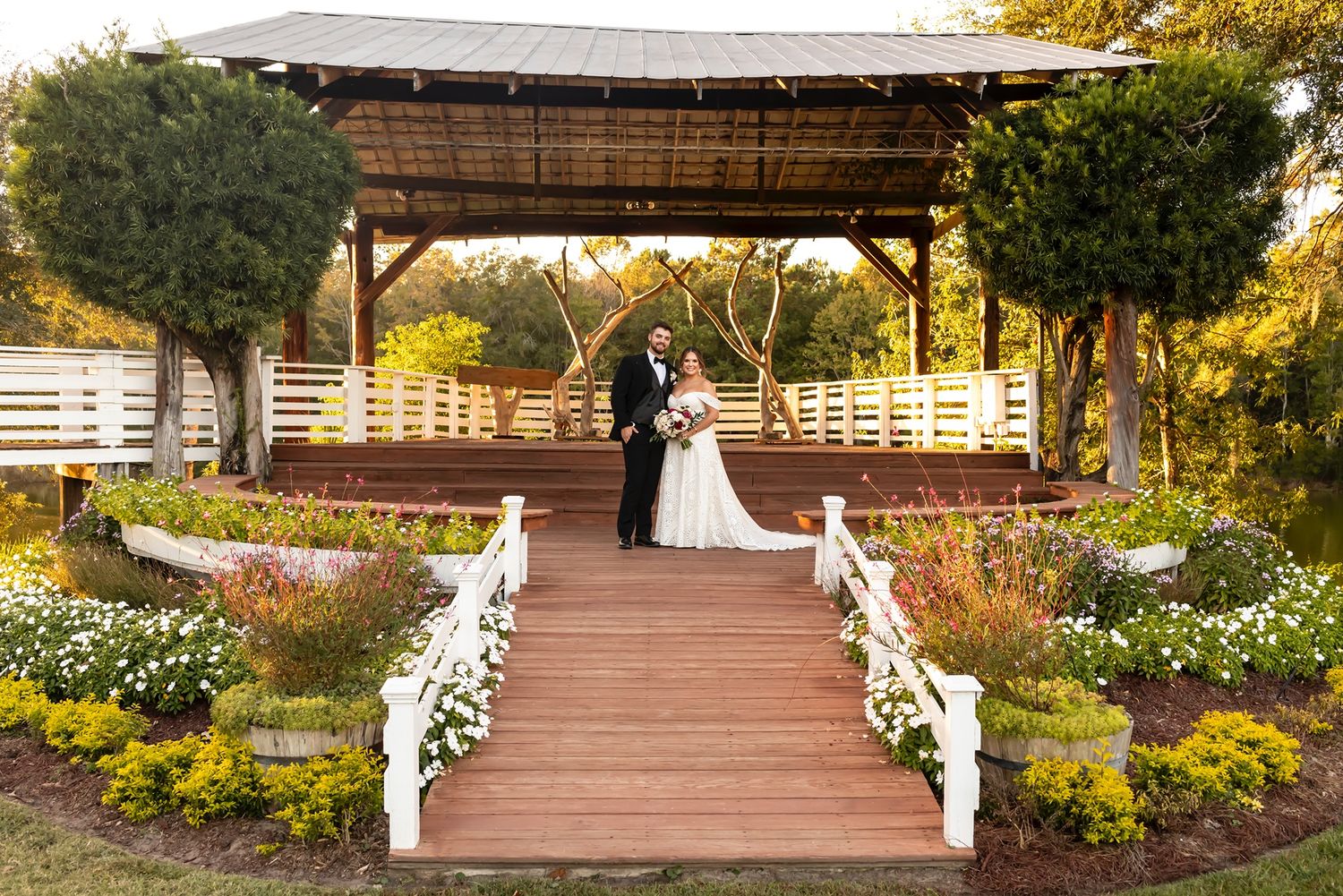 Outdoor wedding ceremony area with white floral arrangements and wooden benches under autumn trees in a garden setting.