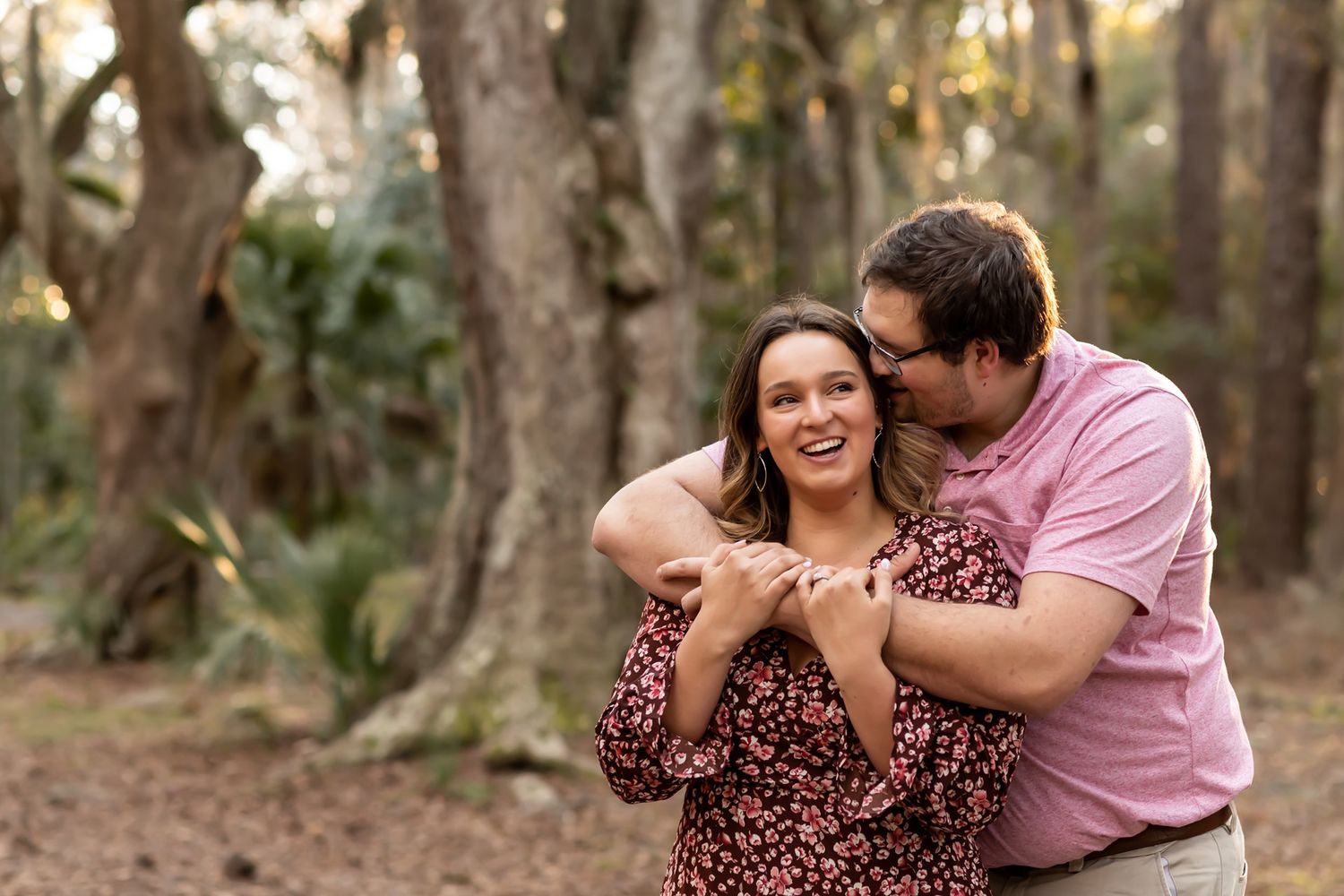A couple in casual attire sharing playful moments and embraces while walking through a wooded outdoor setting.