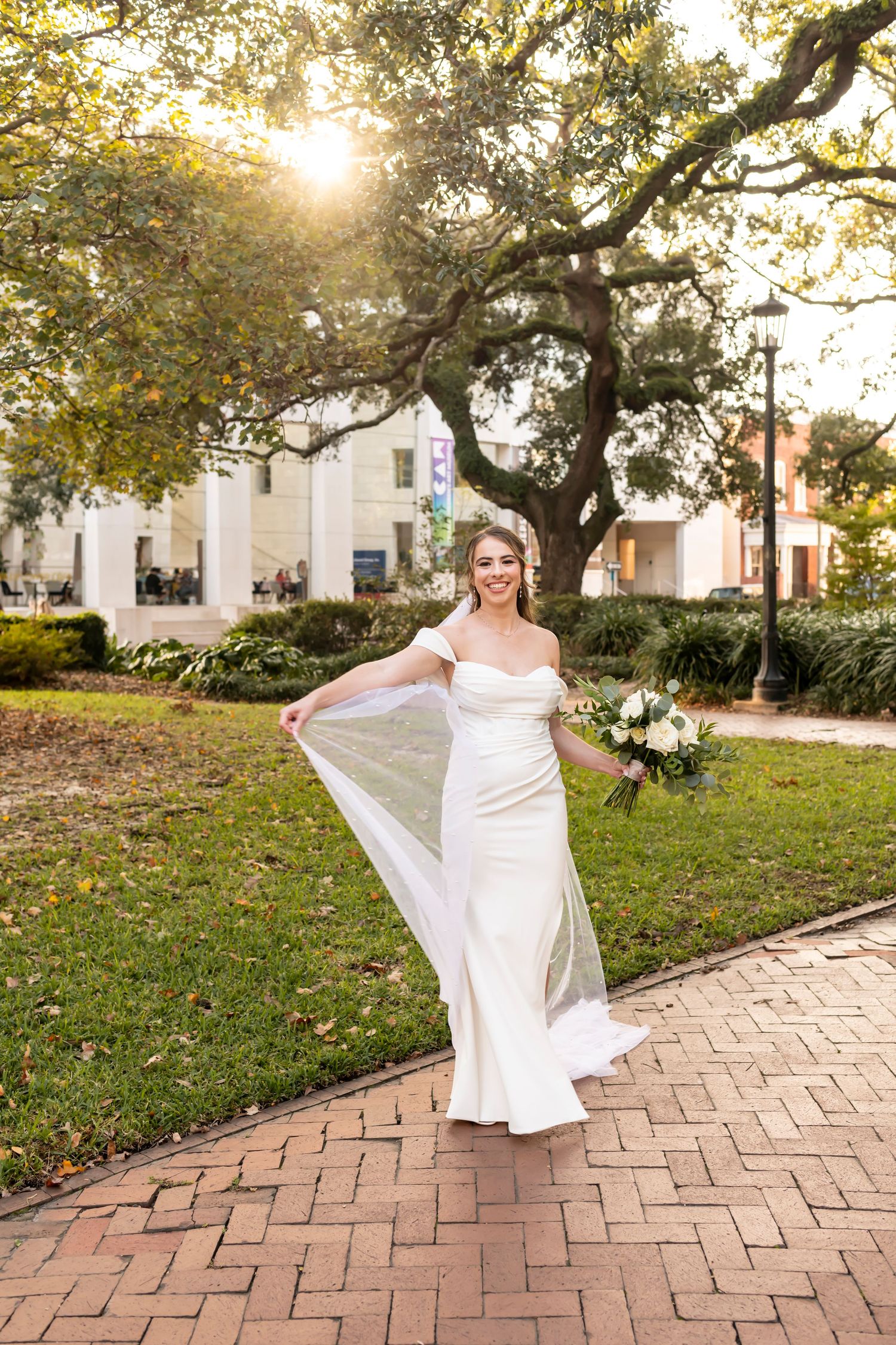 A person in a flowing white dress twirls gracefully on a brick pathway under golden sunlight filtering through oak trees.