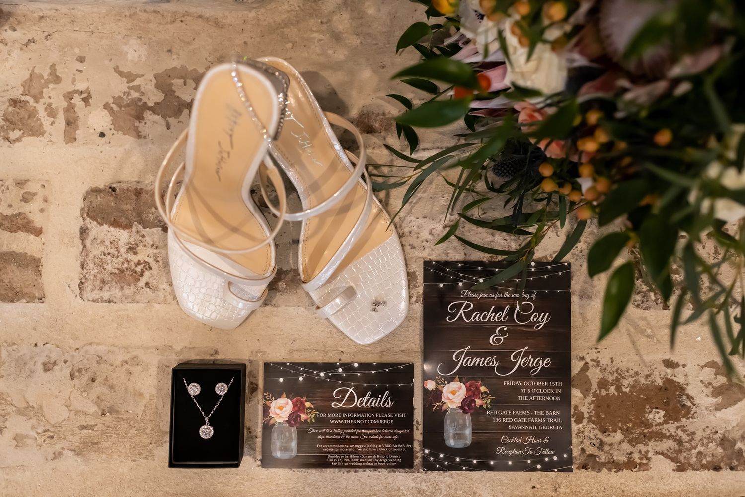 Wedding details including rings, invitations, and floral decor arranged on a rustic stone textured surface.