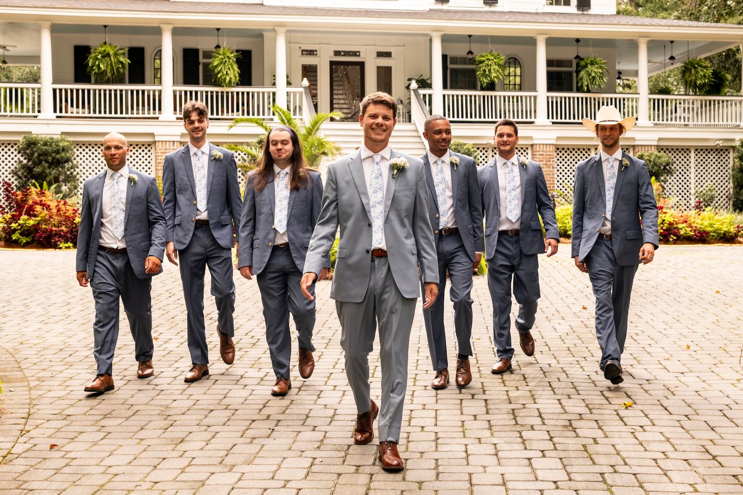 A group of men in grey suits and blue ties walking together on a brick pathway in front of a white columned building.