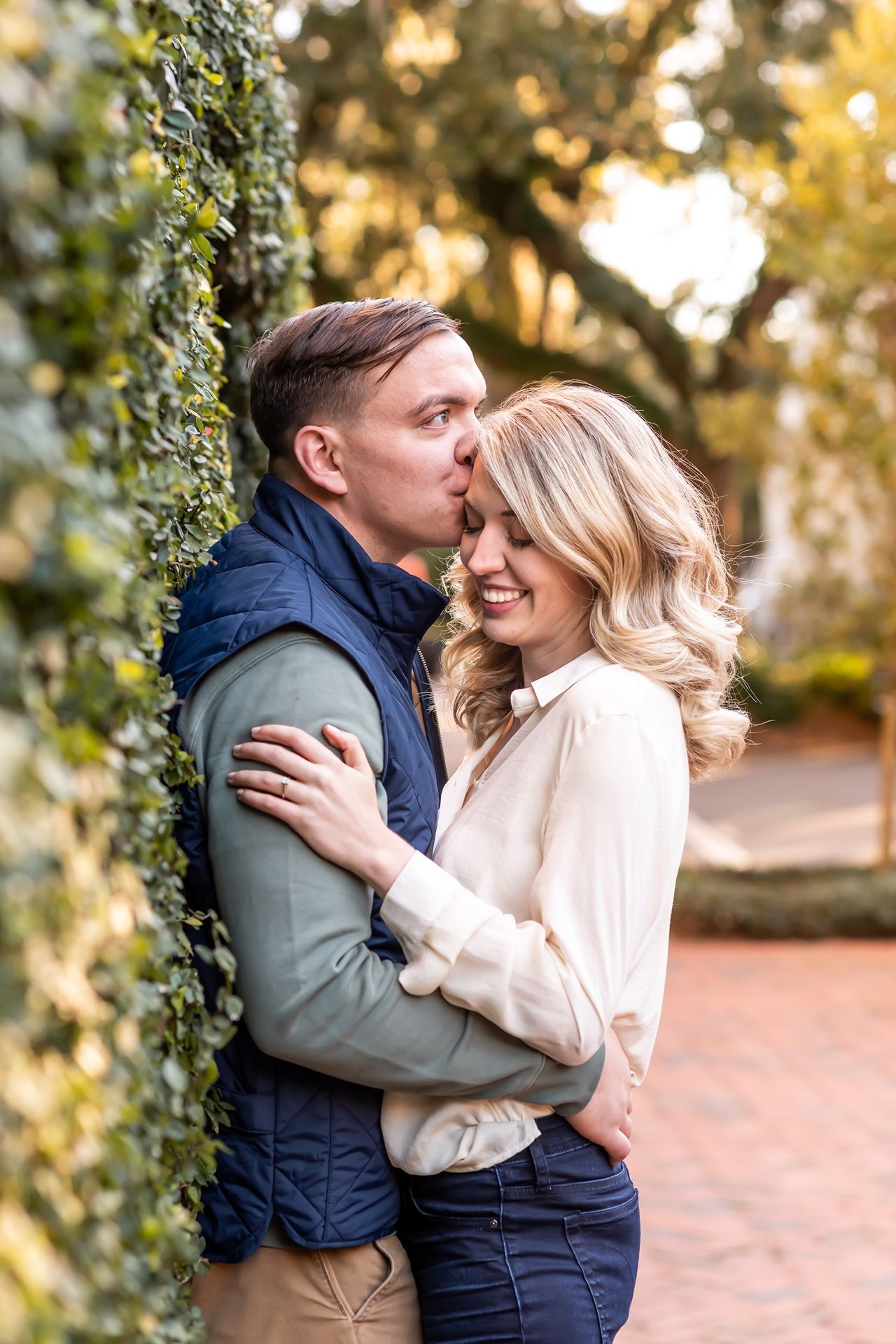 Romantic couple embraces outdoors in autumn with golden sunlight filtering through trees and greenery.