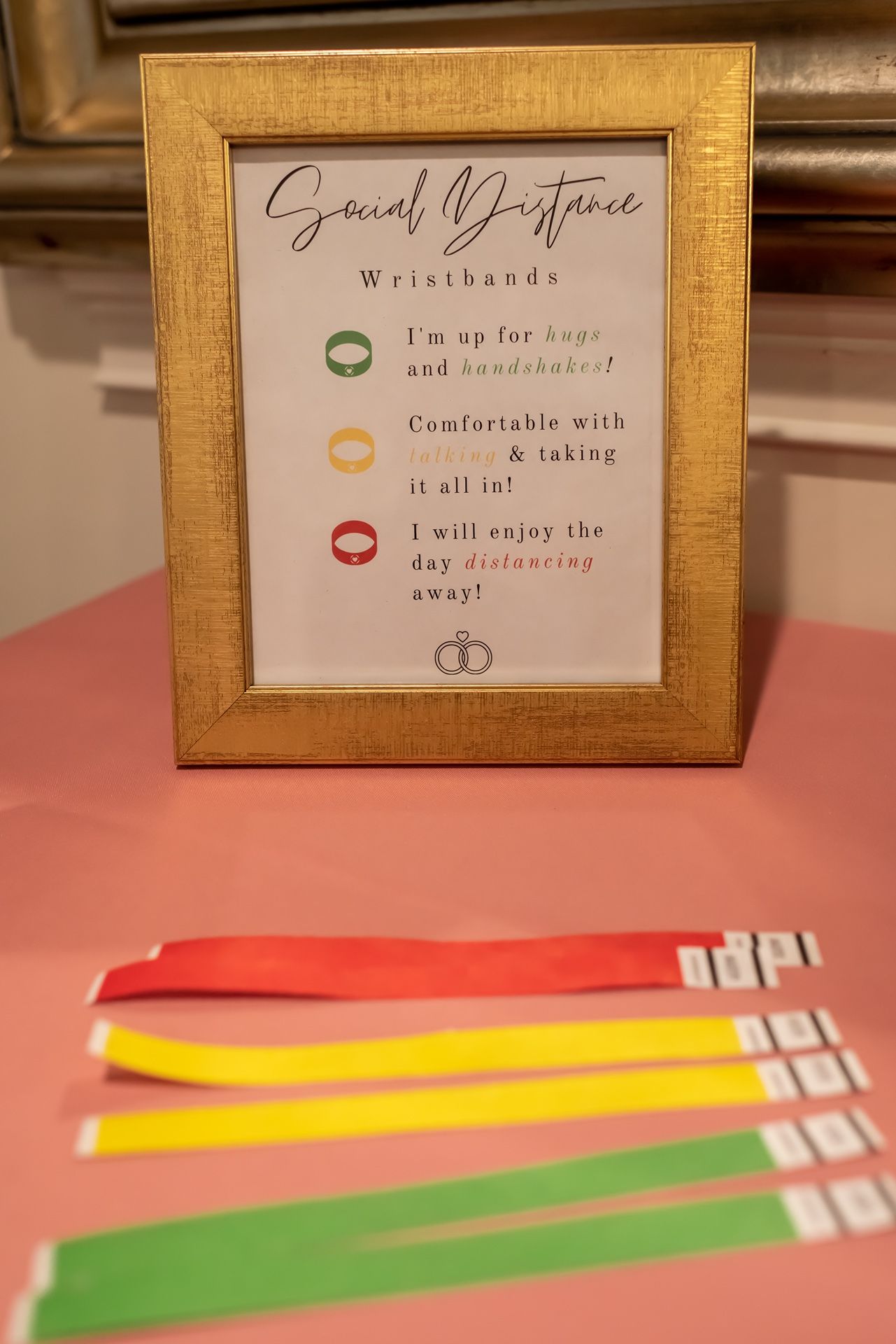 Colored wristbands with social distance indicators displayed on a pink surface next to framed signage.