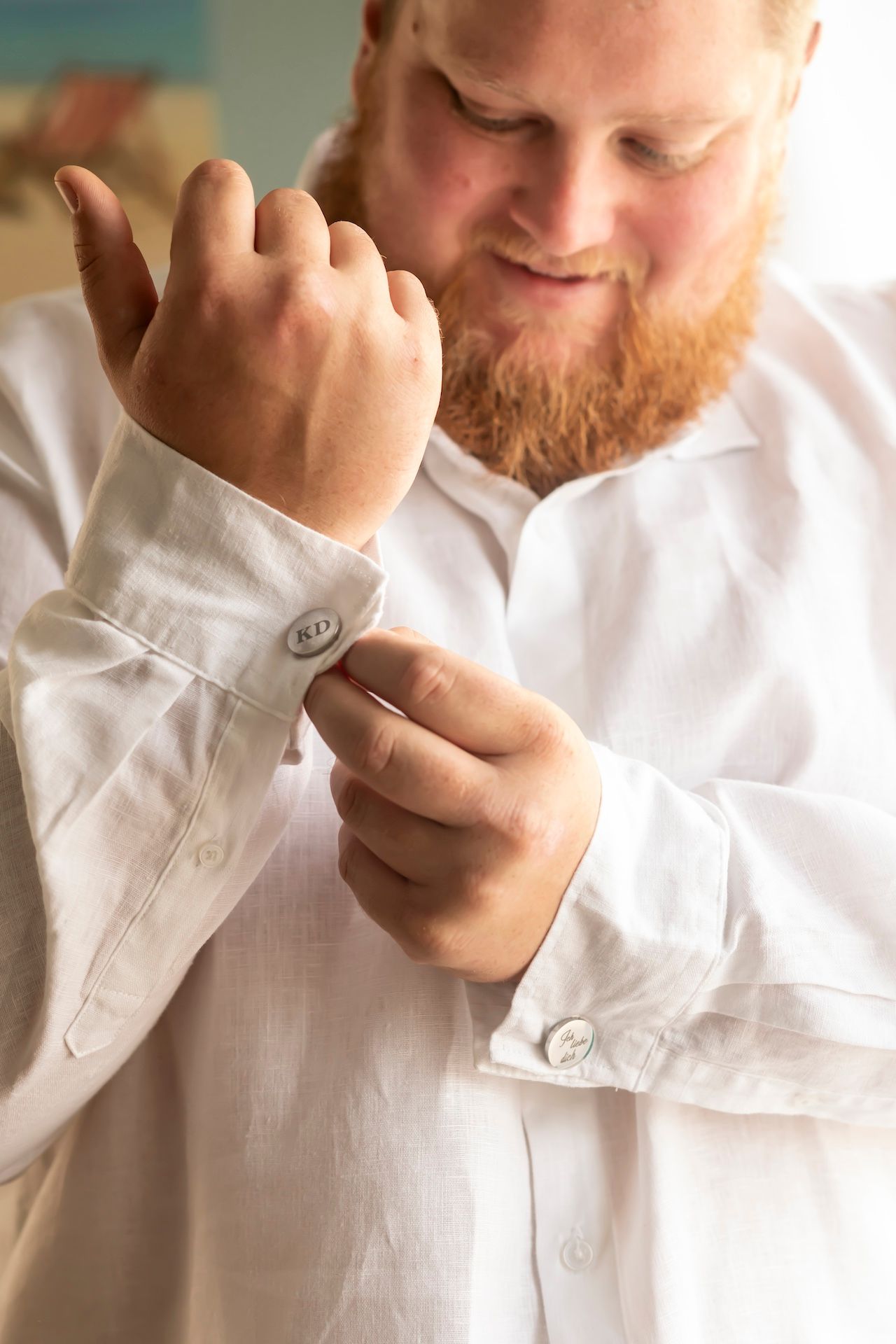 A person in a white button-up shirt adjusts their sleeve cuff while glancing down.