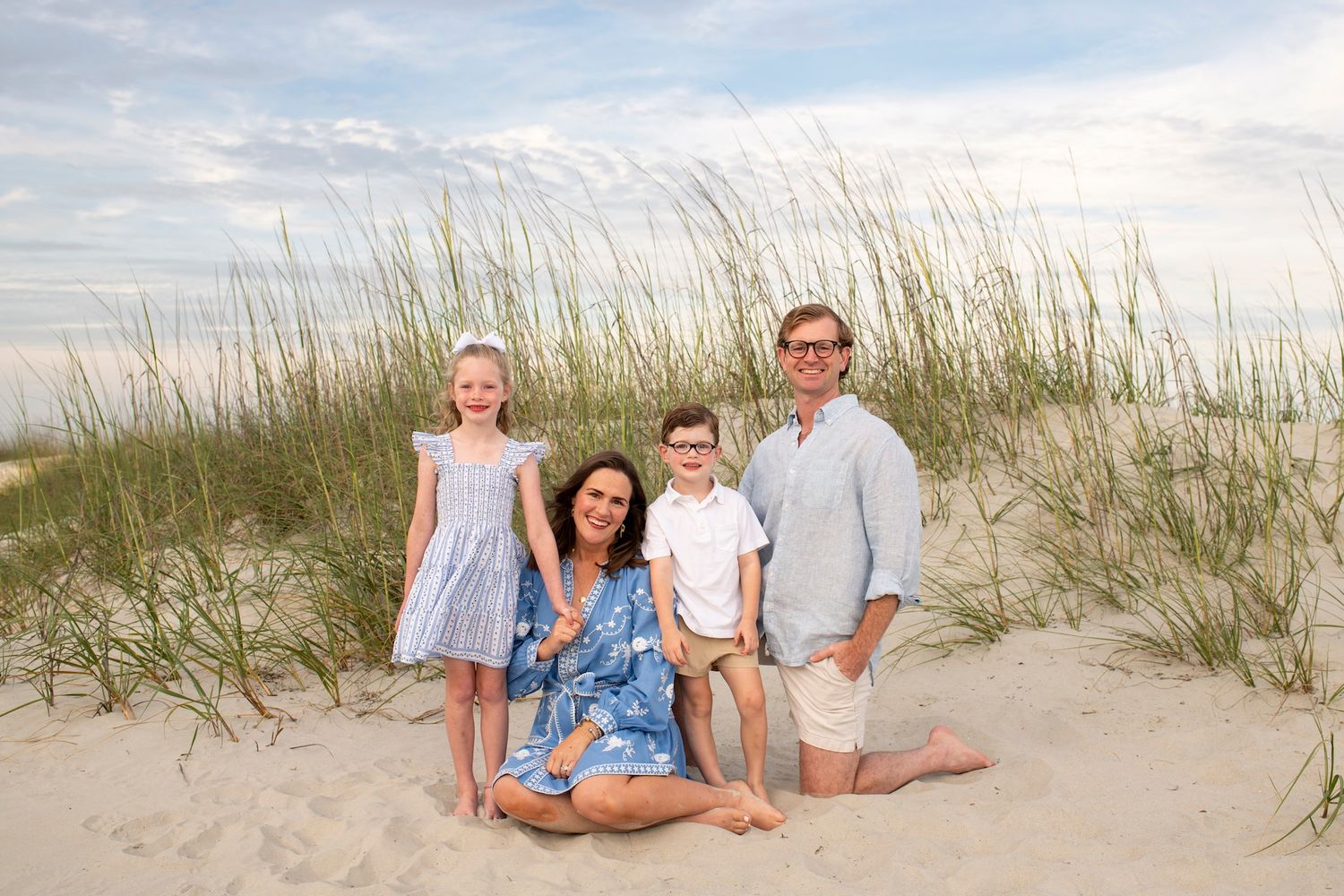 Family of four posing on sandy beach dunes with sea grass on Hilton Head Island beach.
