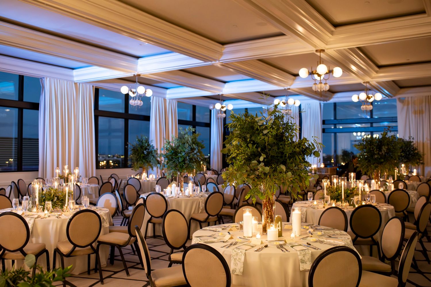 Elegant wedding reception venue with round tables set with white linens and chandeliers in a bright, modern space.