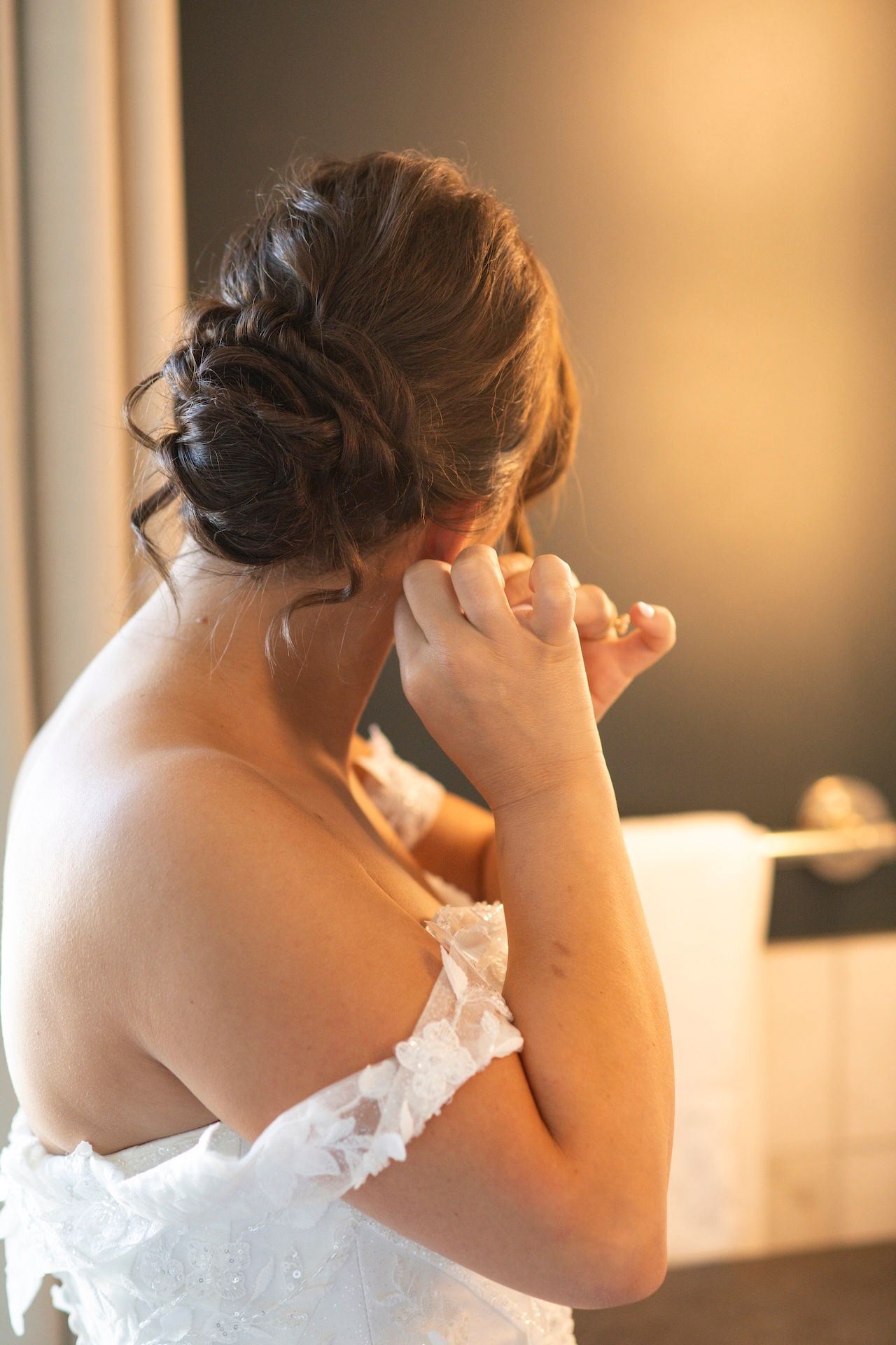 A close-up view of someone wearing a white wedding dress with their hand raised to their face.