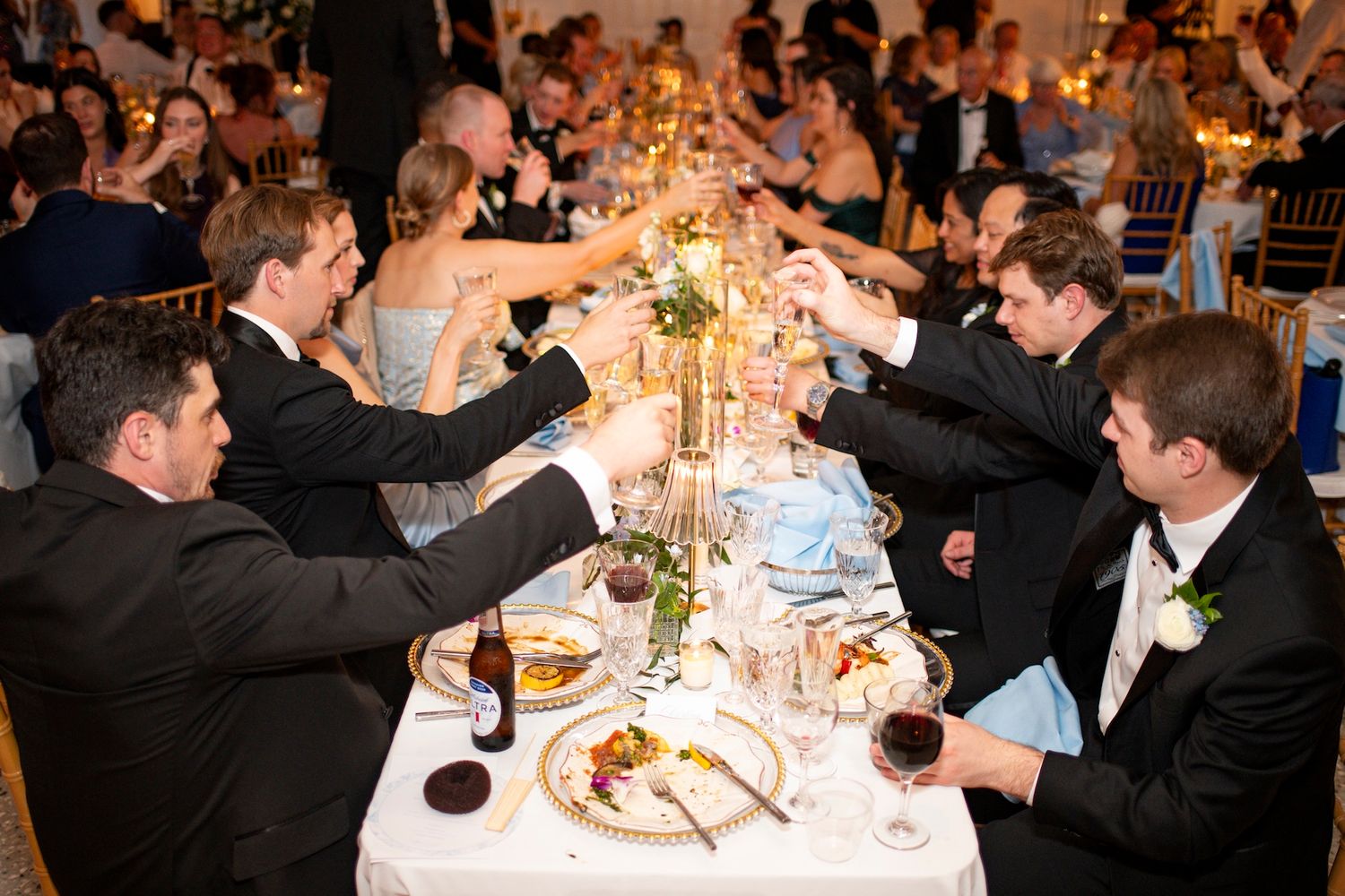 Guests raising glasses in a toast at an elegant wedding reception dinner table with candles and fine dining.
