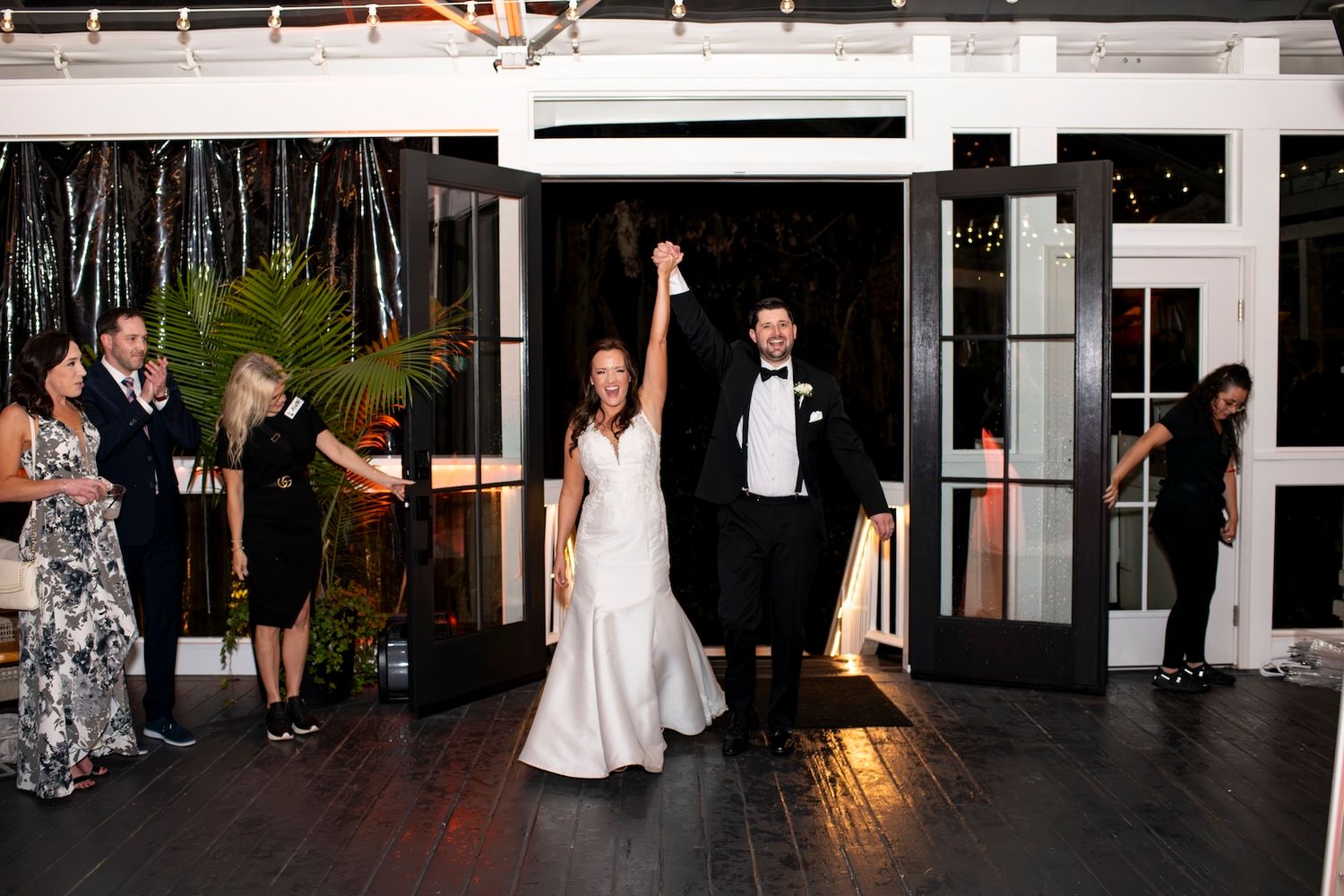 Bride and groom raise hands in triumphant grand entrance at elegant wedding reception venue.