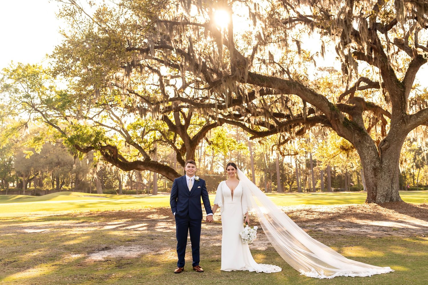 A romantic wedding portrait under a majestic Spanish moss-draped oak tree during golden hour in a Southern garden.