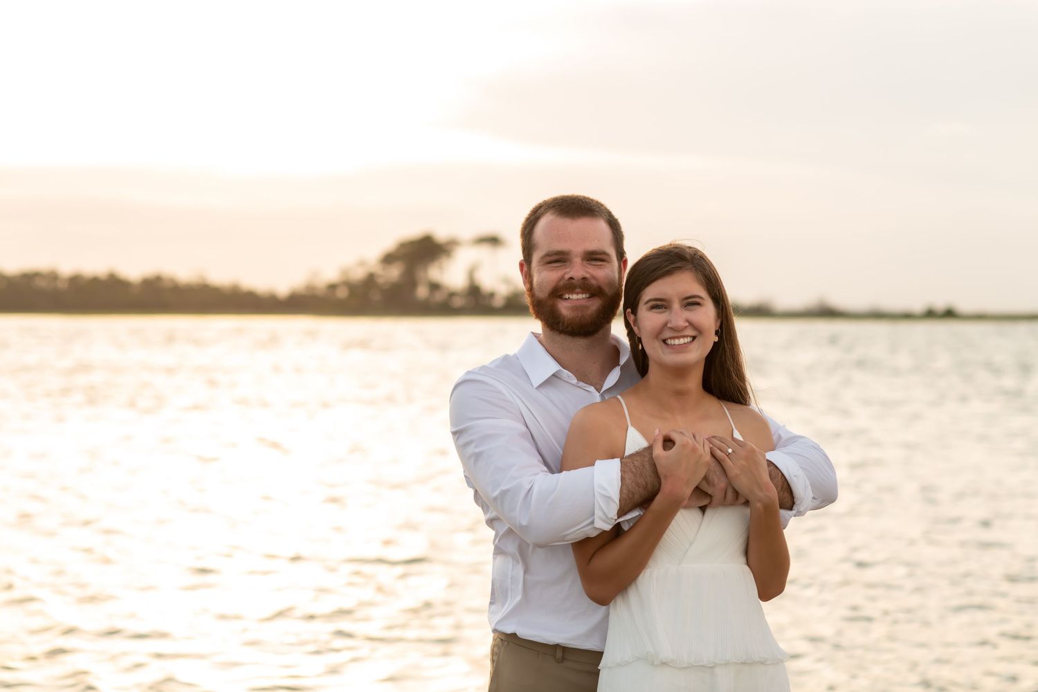 A romantic sunset beach photoshoot shows a couple embracing on the sandy shore with golden light glowing behind them.