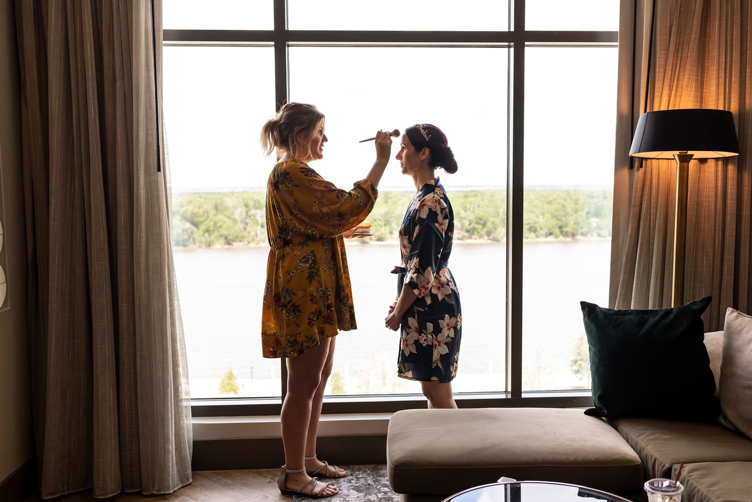 Two people stand silhouetted by natural light streaming through tall windows in an elegant room.