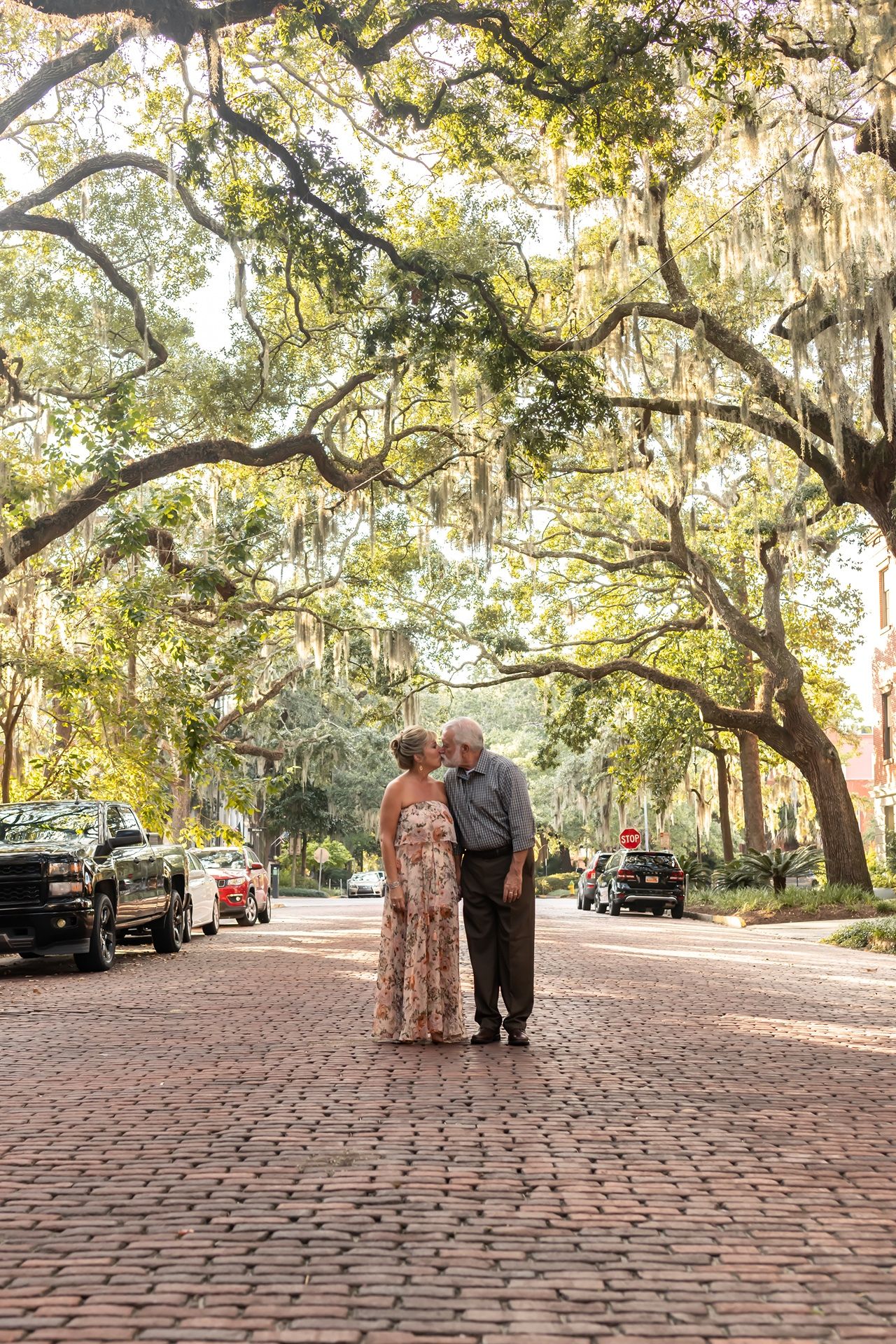 A couple embraces on a romantic brick-paved street lined with Spanish moss-draped oak trees in Savannah, Georgia.