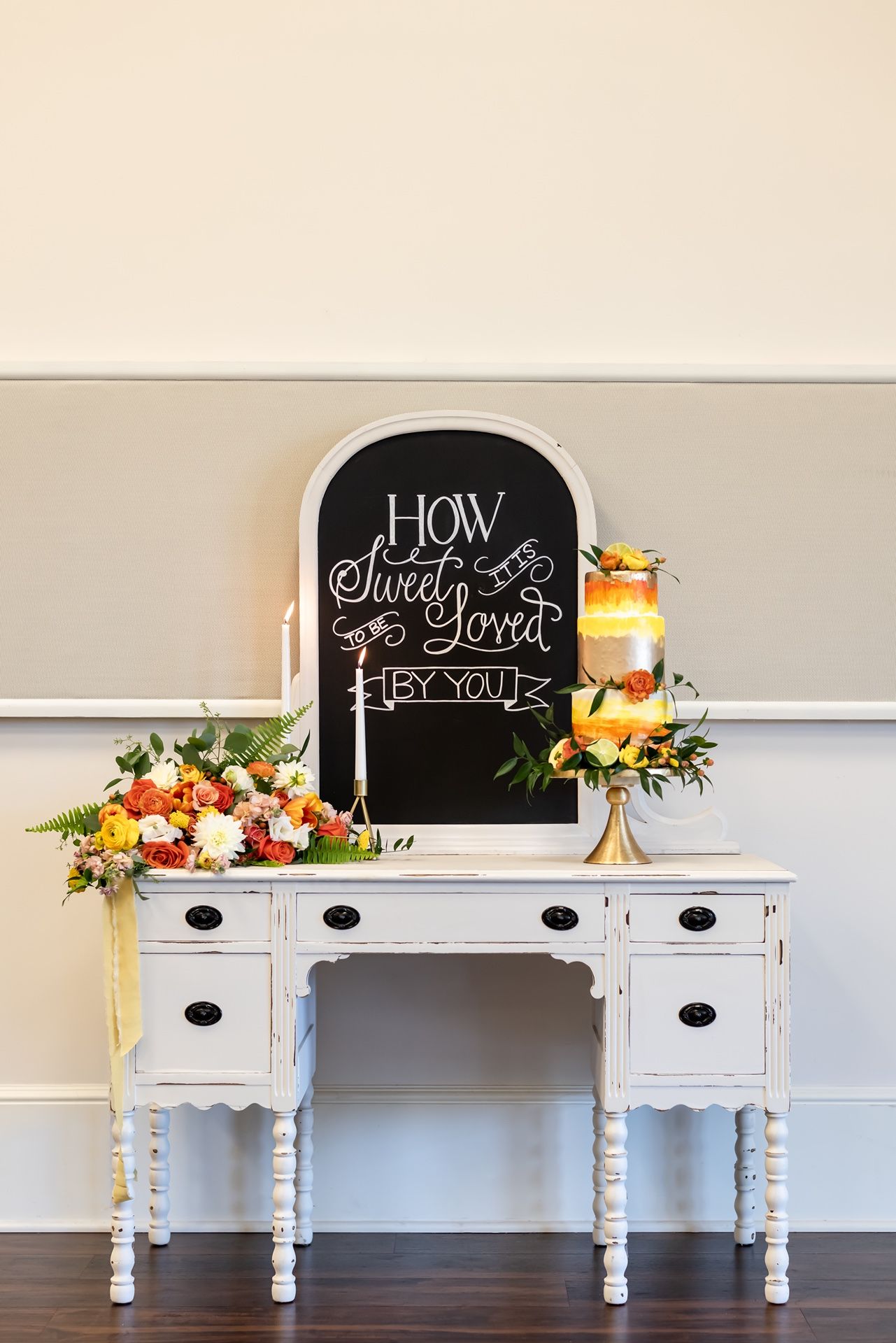 White vintage console table with chalkboard signs and floral decorations displayed at varying angles against grey wall.