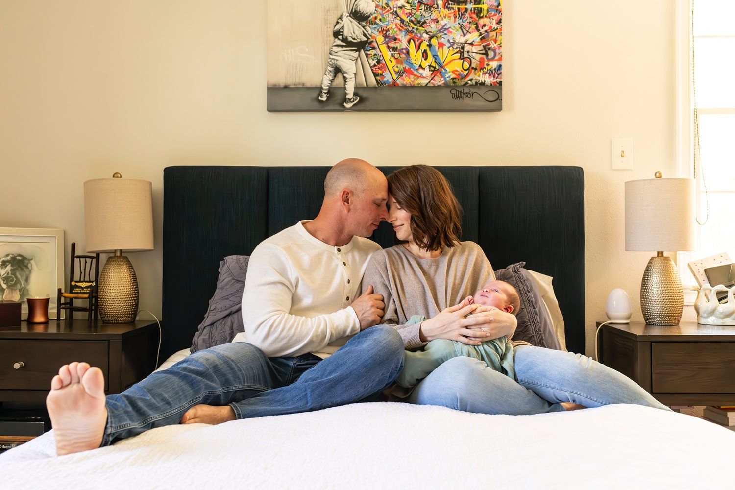 Couple relaxing together on bed in casual clothing with colorful artwork on wall behind them.