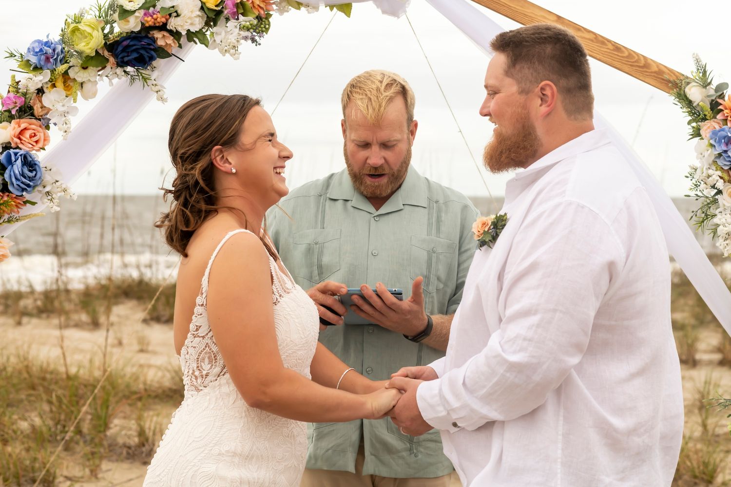 A beachside wedding ceremony under a floral arch with soft sunlight illuminating the romantic moment.