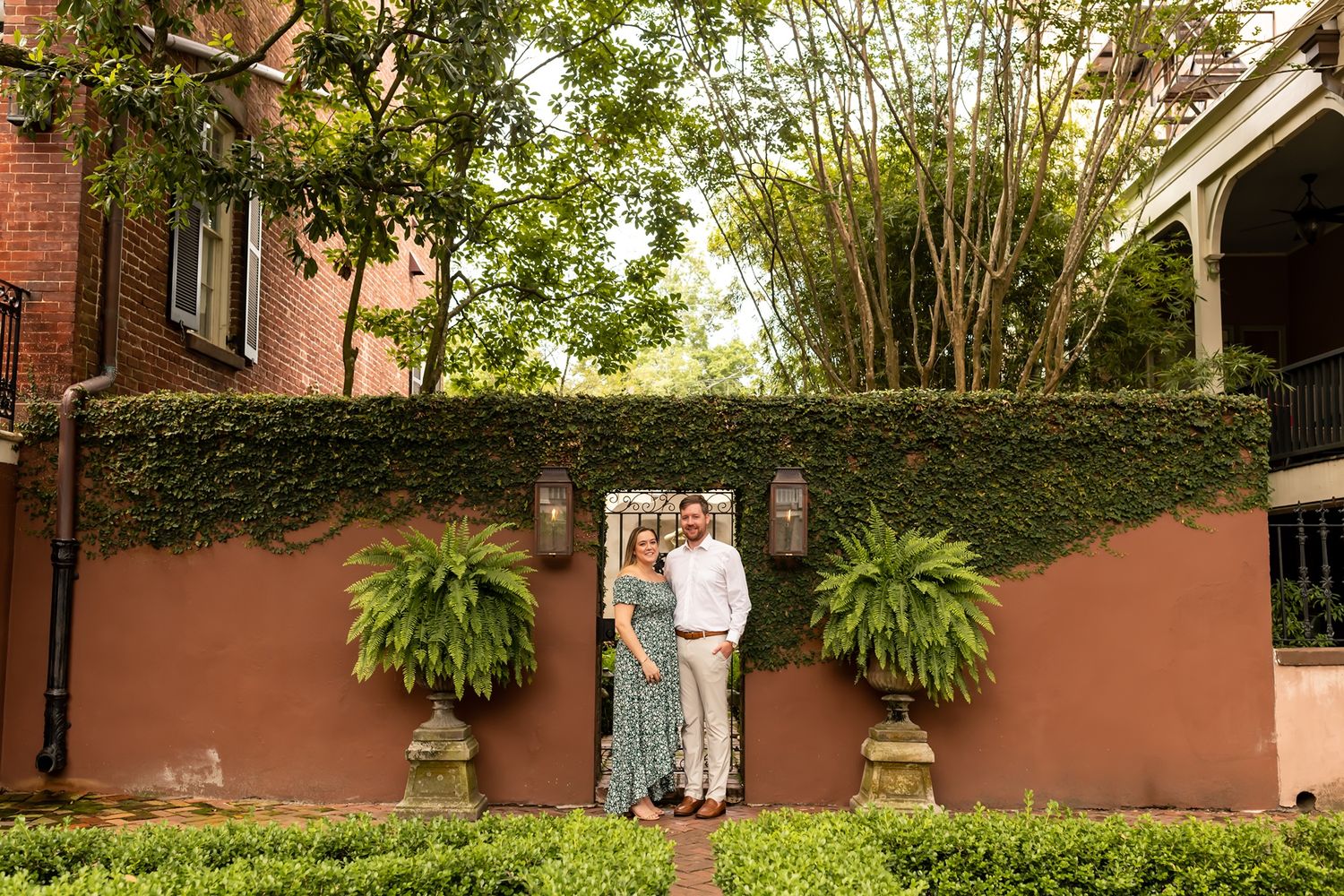 Three people stand in front of a coral-colored wall covered in ivy with hanging ferns in decorative planters.