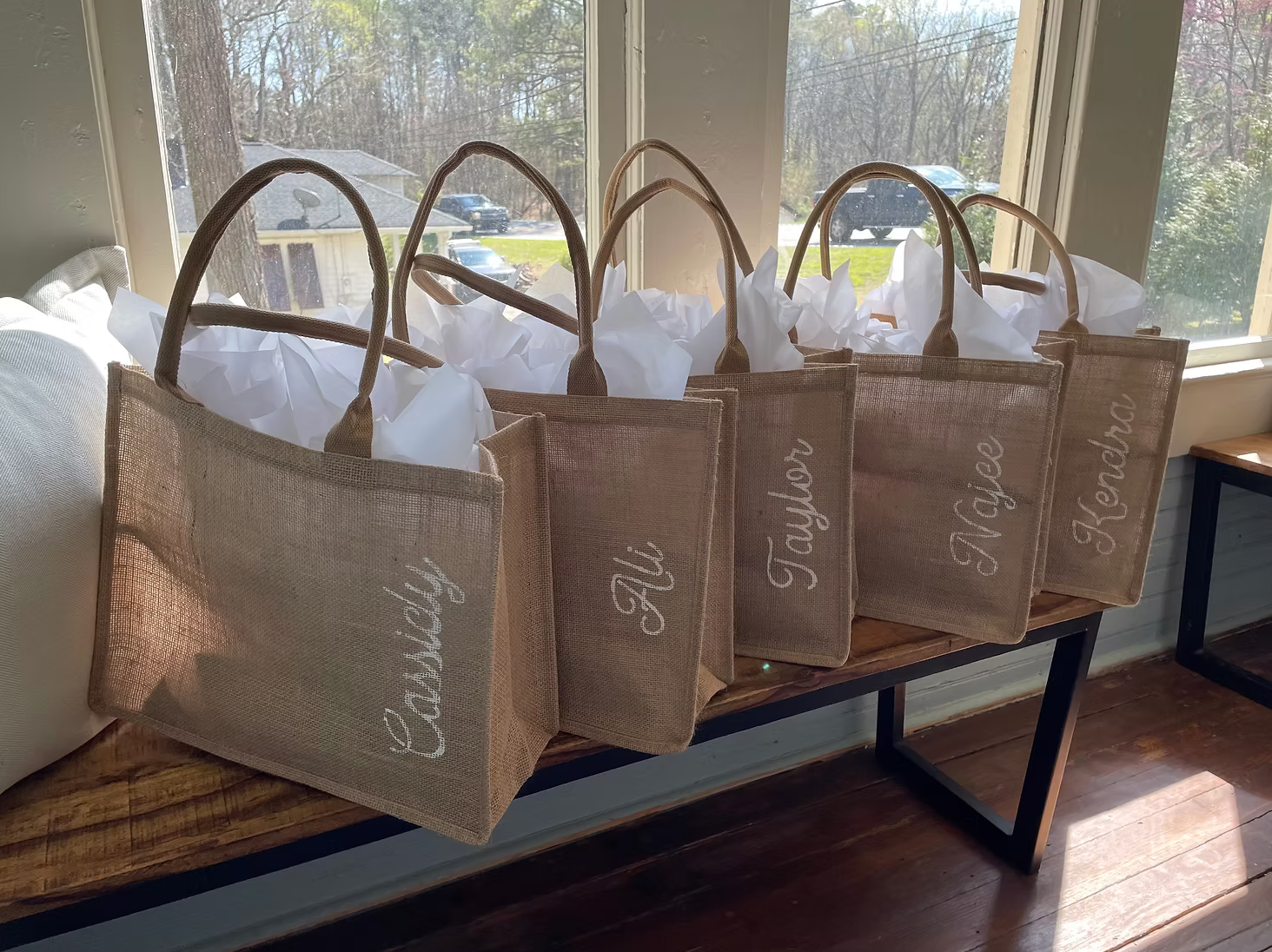 A row of brown paper gift bags with hand-lettered numbers sit lined up on a white windowsill in natural light.