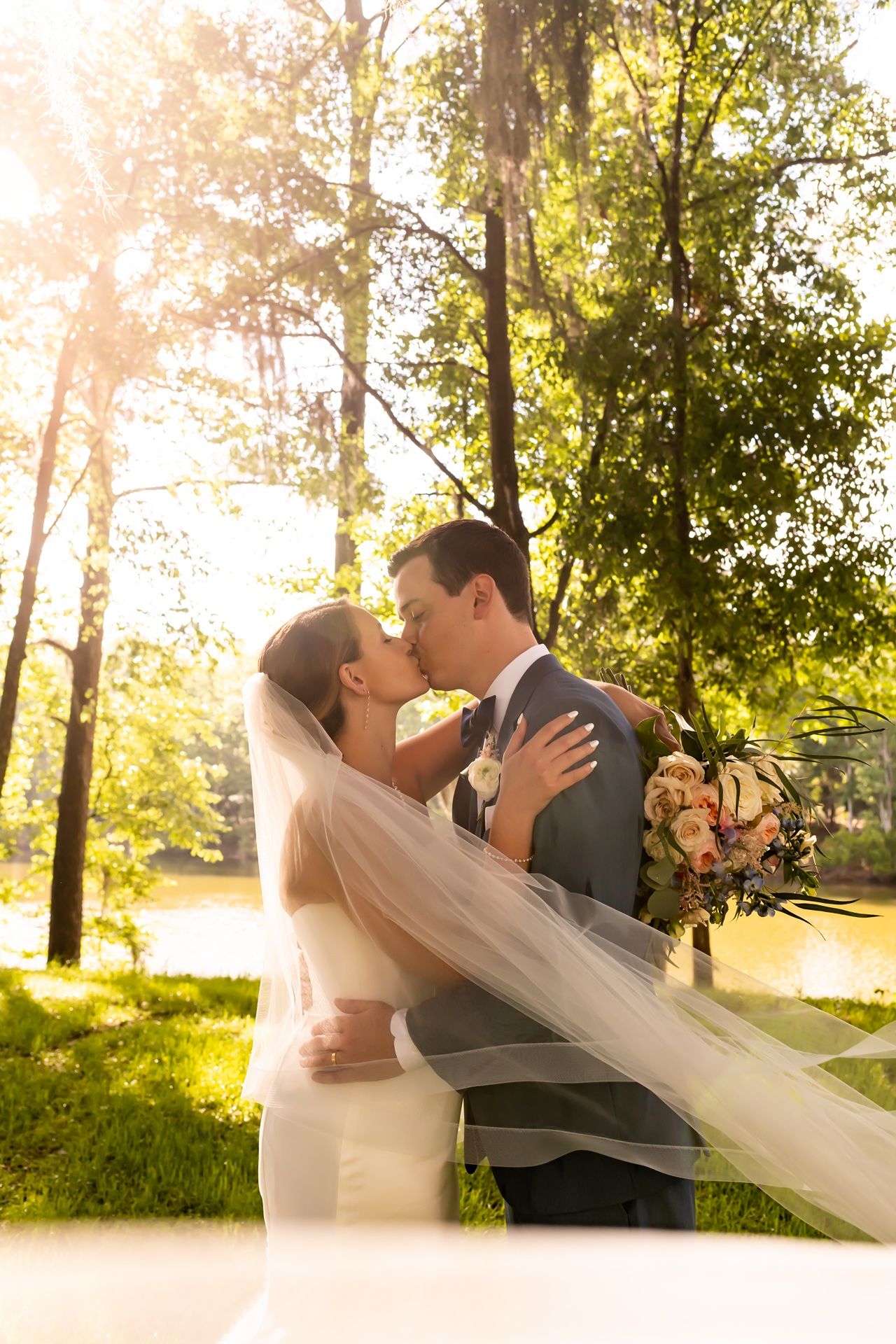 A romantic golden hour wedding scene with dancing and flowing veil as light glows through trees in a park setting.
