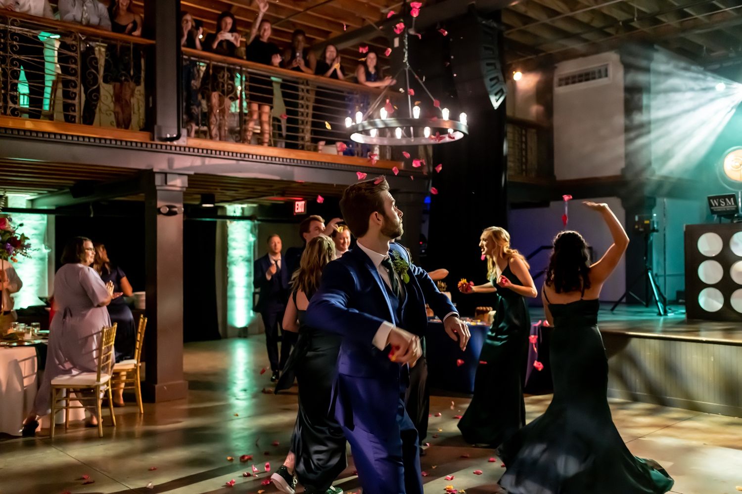 Wedding guests dancing together on a dimly lit dance floor at an evening reception celebration.