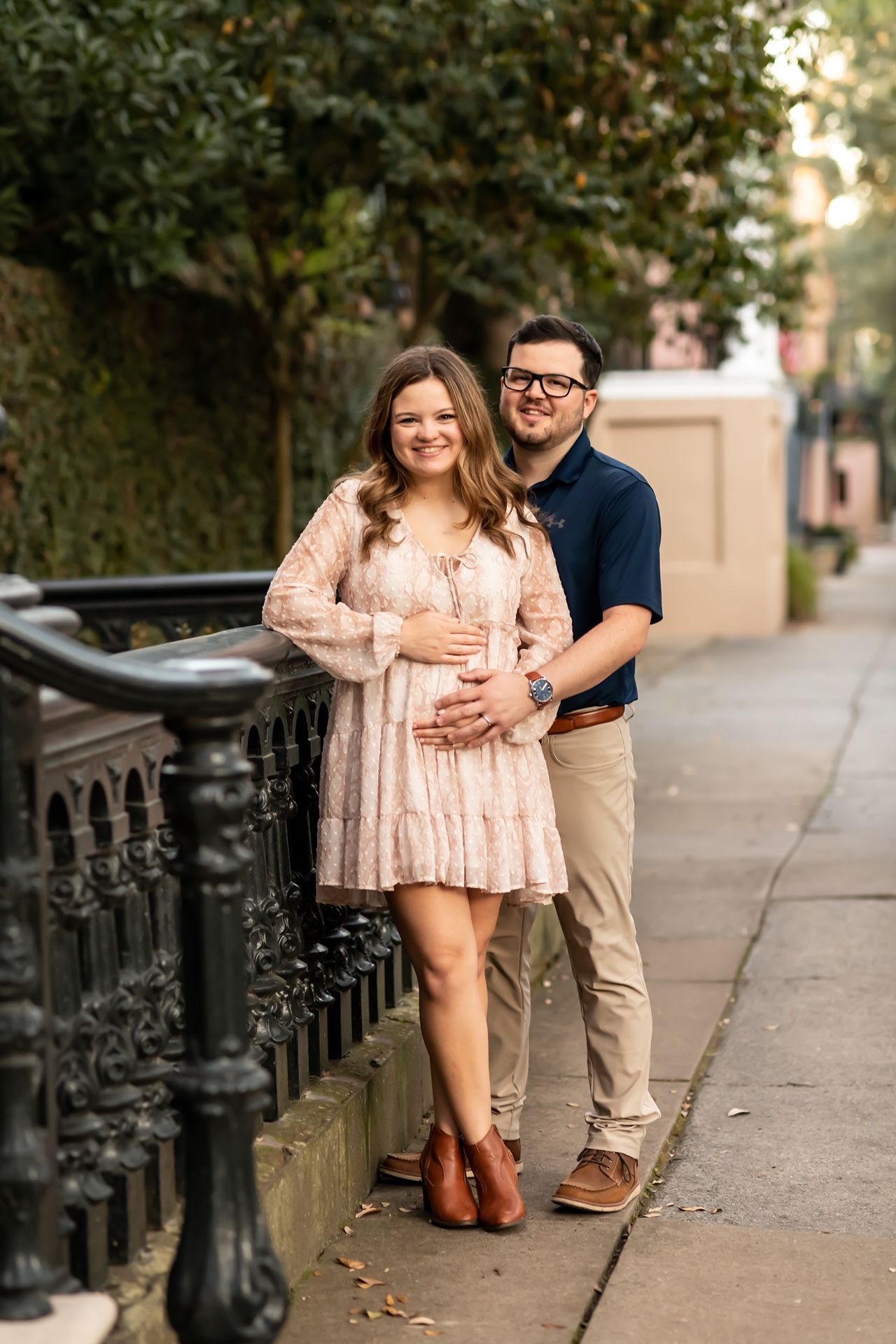A couple sits together on steps during a sunset photo session beside decorative iron railings in an urban setting.