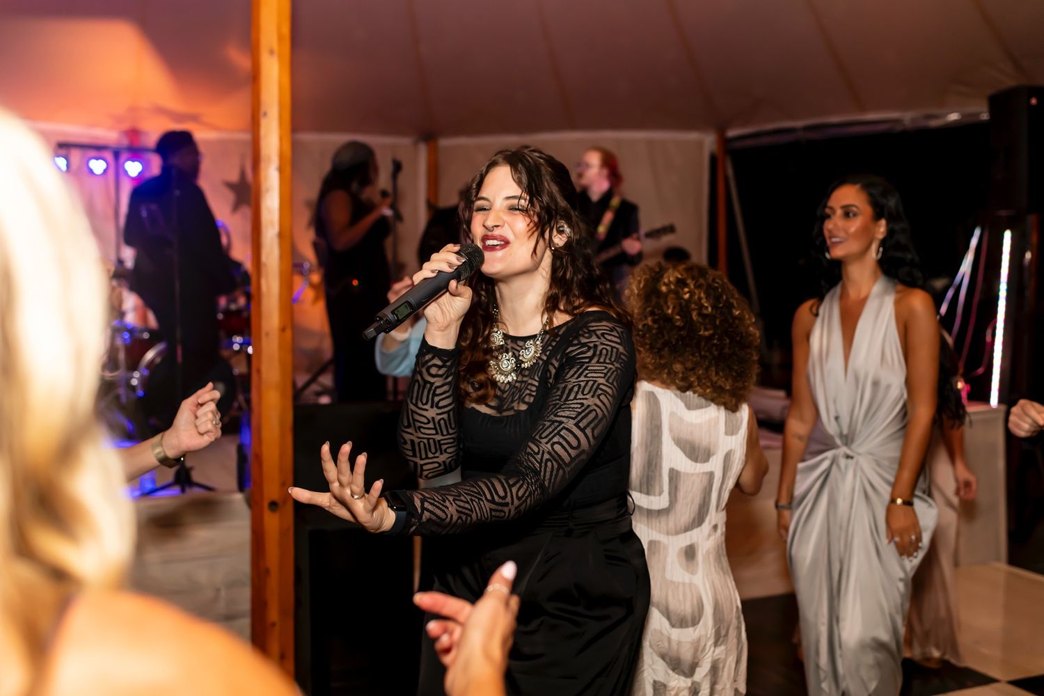 A person in a black lace dress dances energetically at a party event under ambient lighting with other guests nearby.