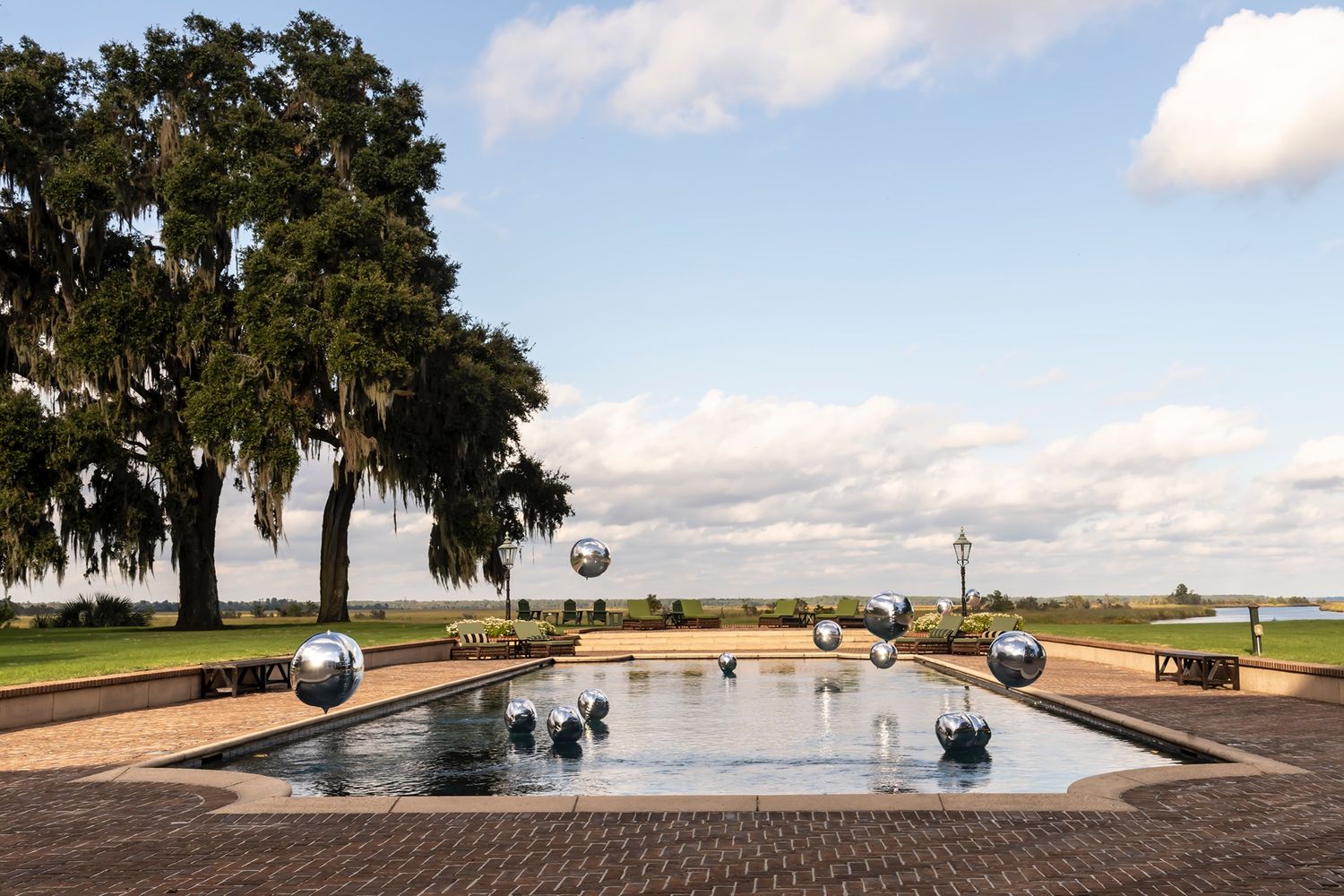 A large reflecting pool surrounded by brick pavers and oak trees with hanging moss.