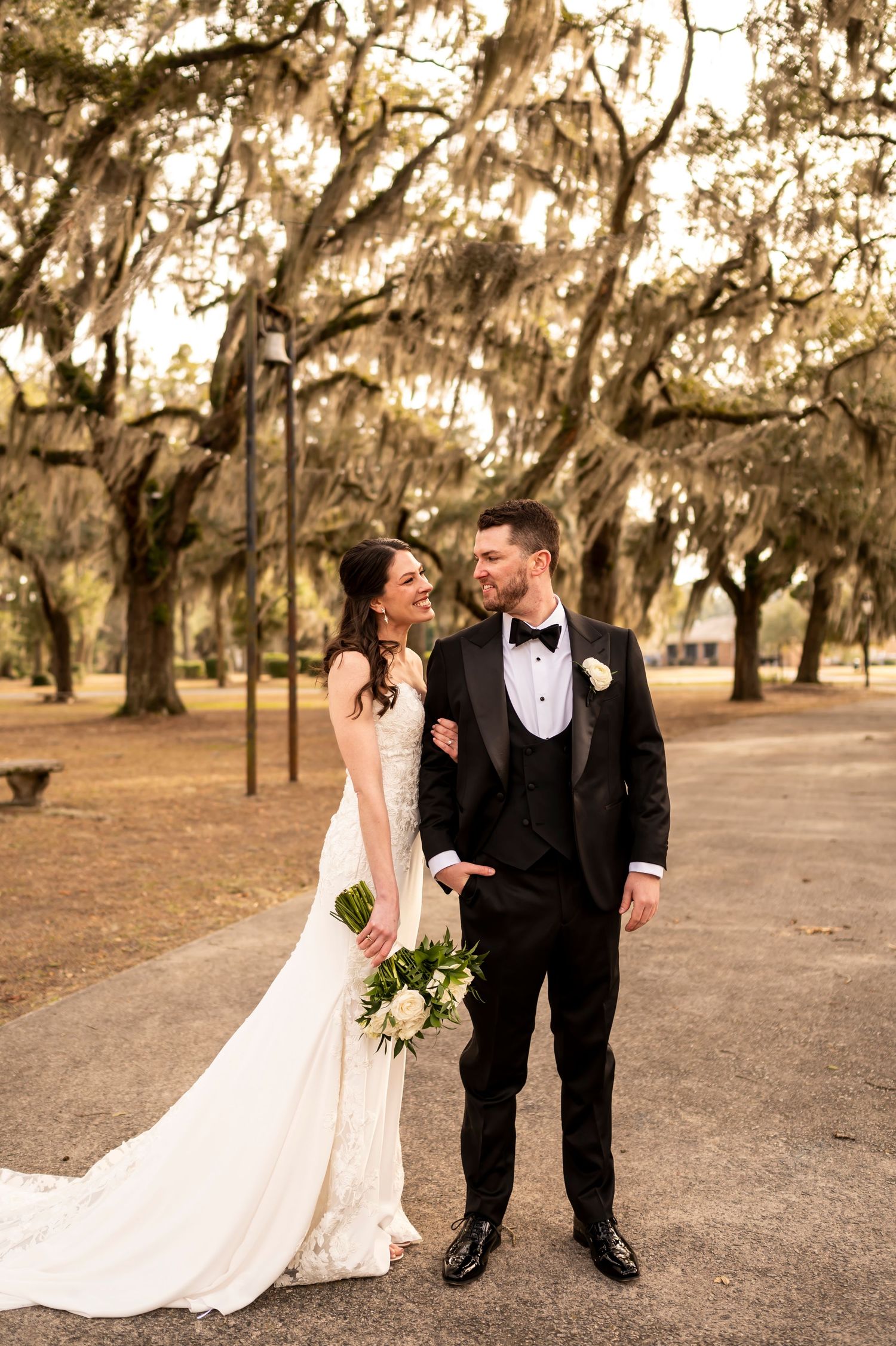 A couple shares a joyful moment under moss-draped oak trees in a romantic outdoor setting.