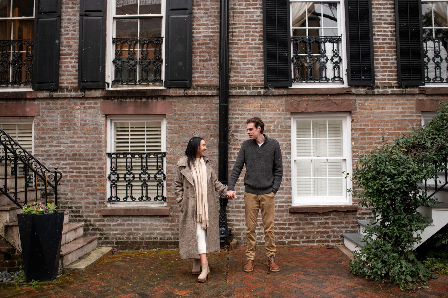 A couple stands together on a brick sidewalk in a rare snow in Savannah, Georgia for the post proposal photos.