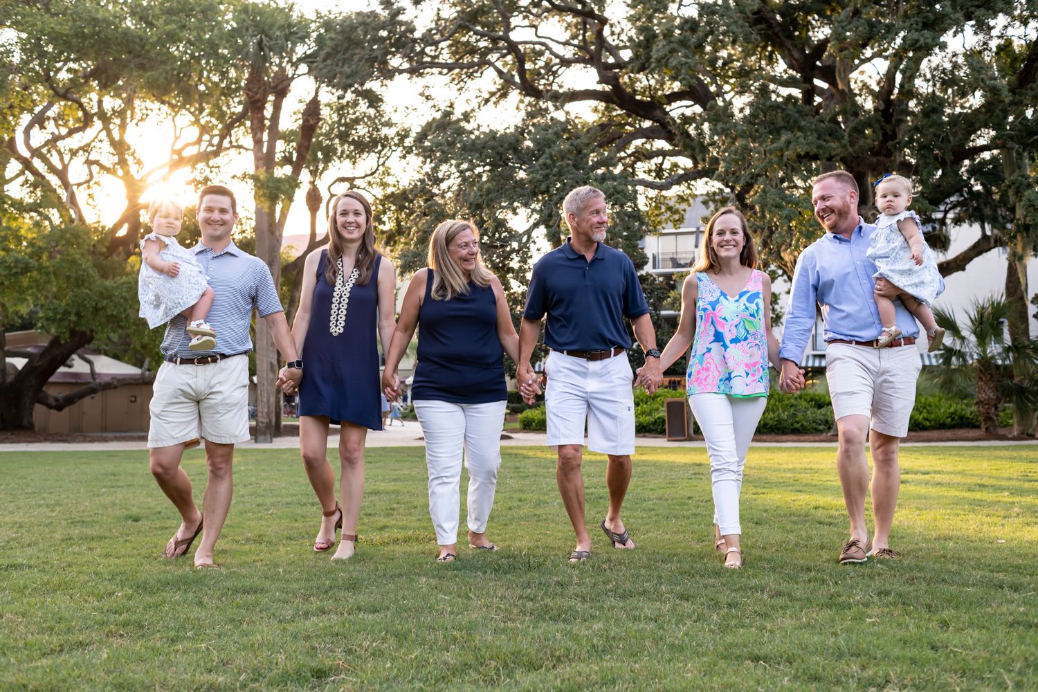 Family group walking together in white and navy outfits during golden hour outdoor photo session at a park.