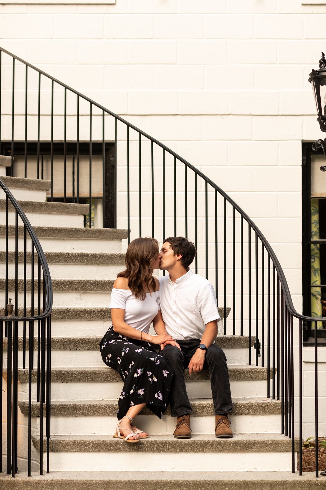 A couple sitting and relaxing together on white concrete steps with black metal railings.