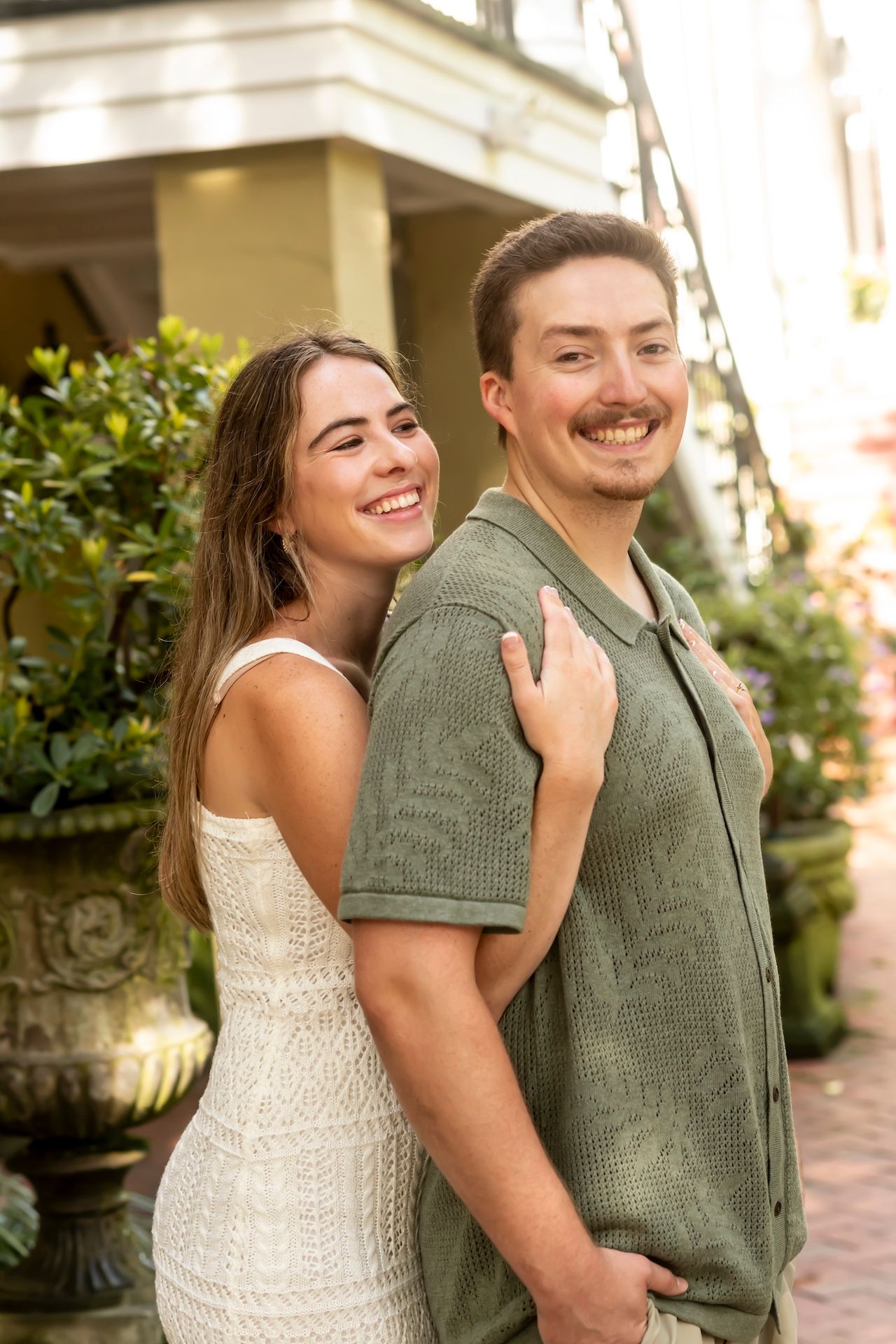 A happy couple sharing a joyful moment together outside, with her in a white dress and him wearing a green shirt.