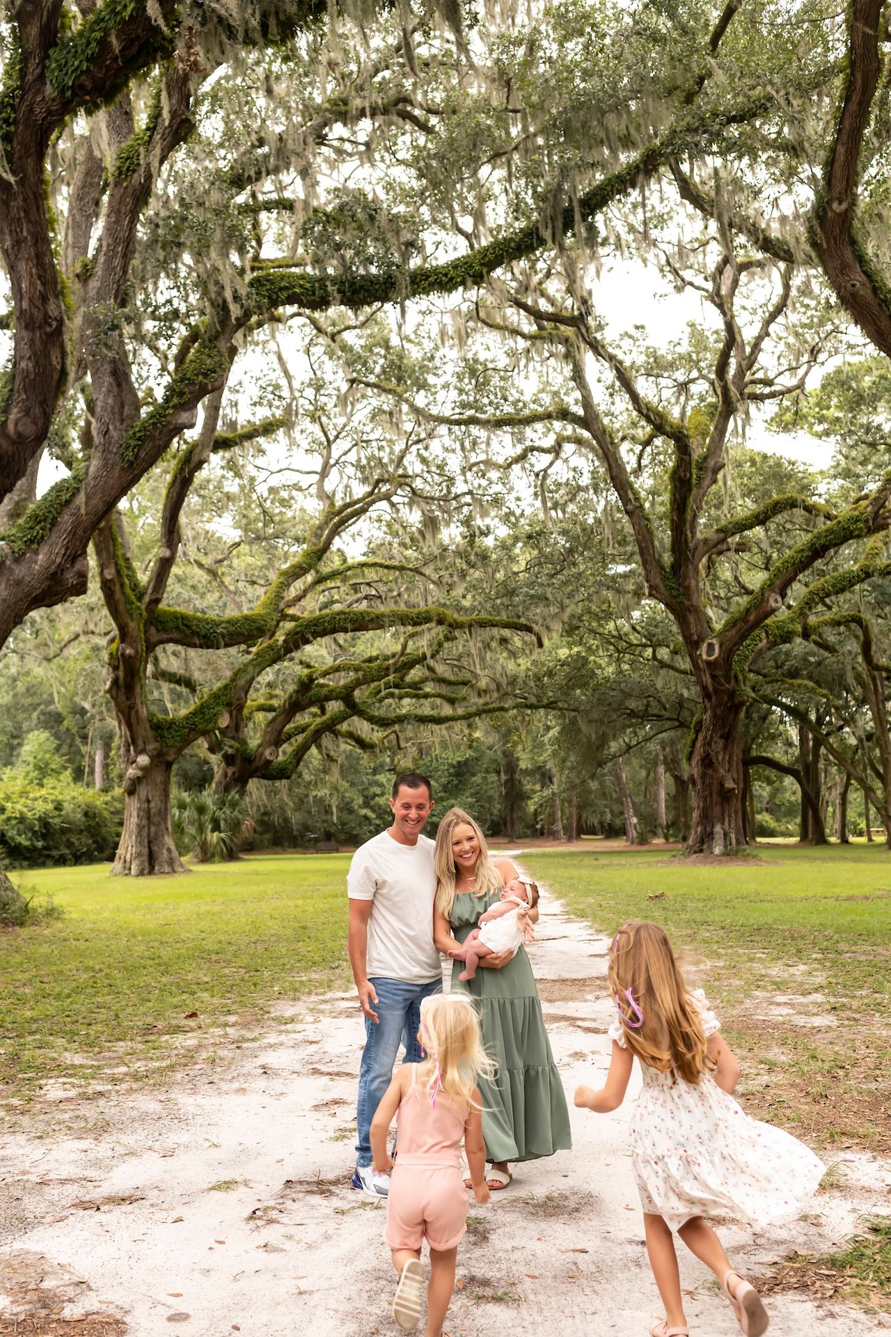 A family enjoying a walk along a sandy path beneath majestic Spanish moss draped oak trees in a Southern park.