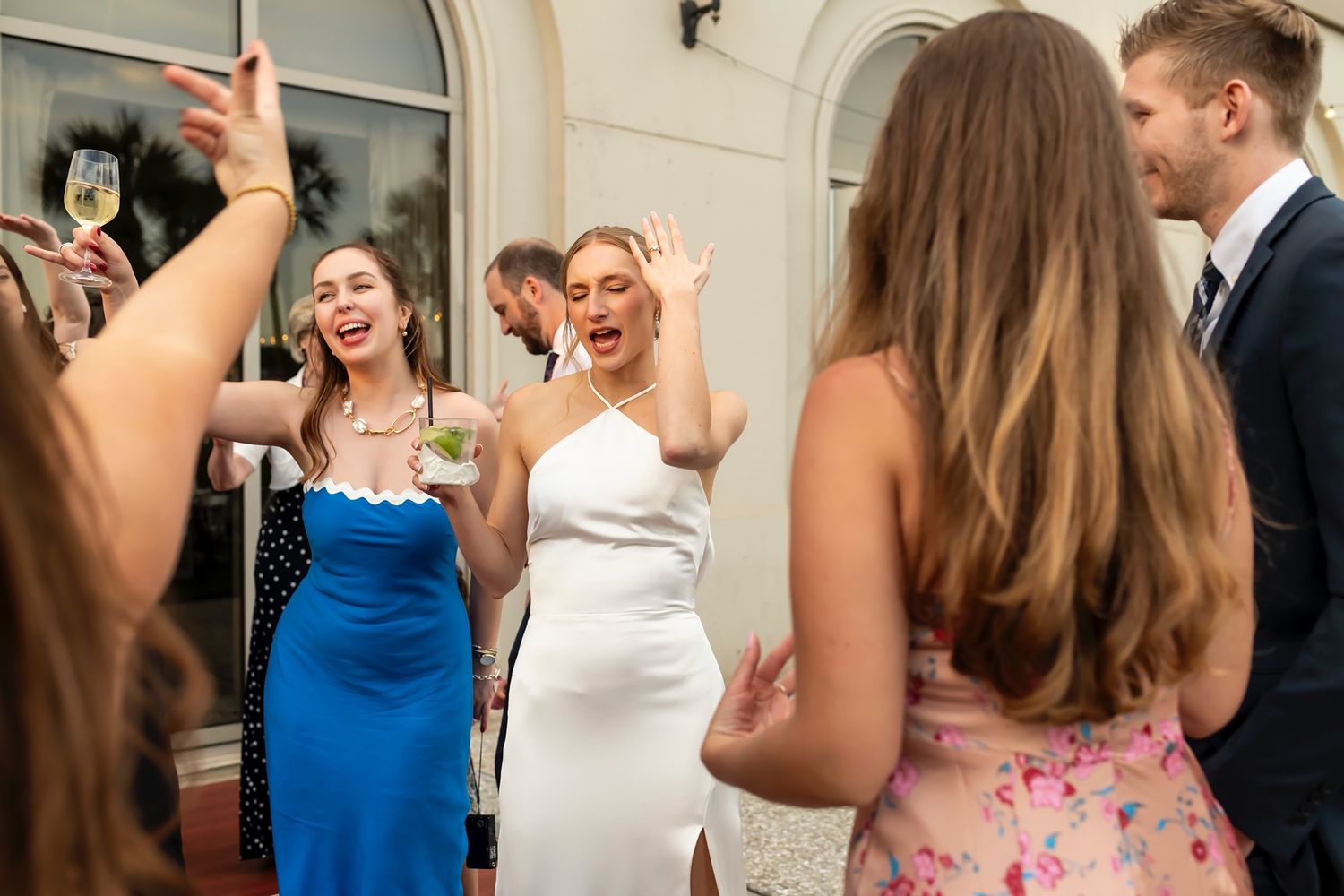 Wedding guests in colorful attire celebrate and dance joyfully during a reception.