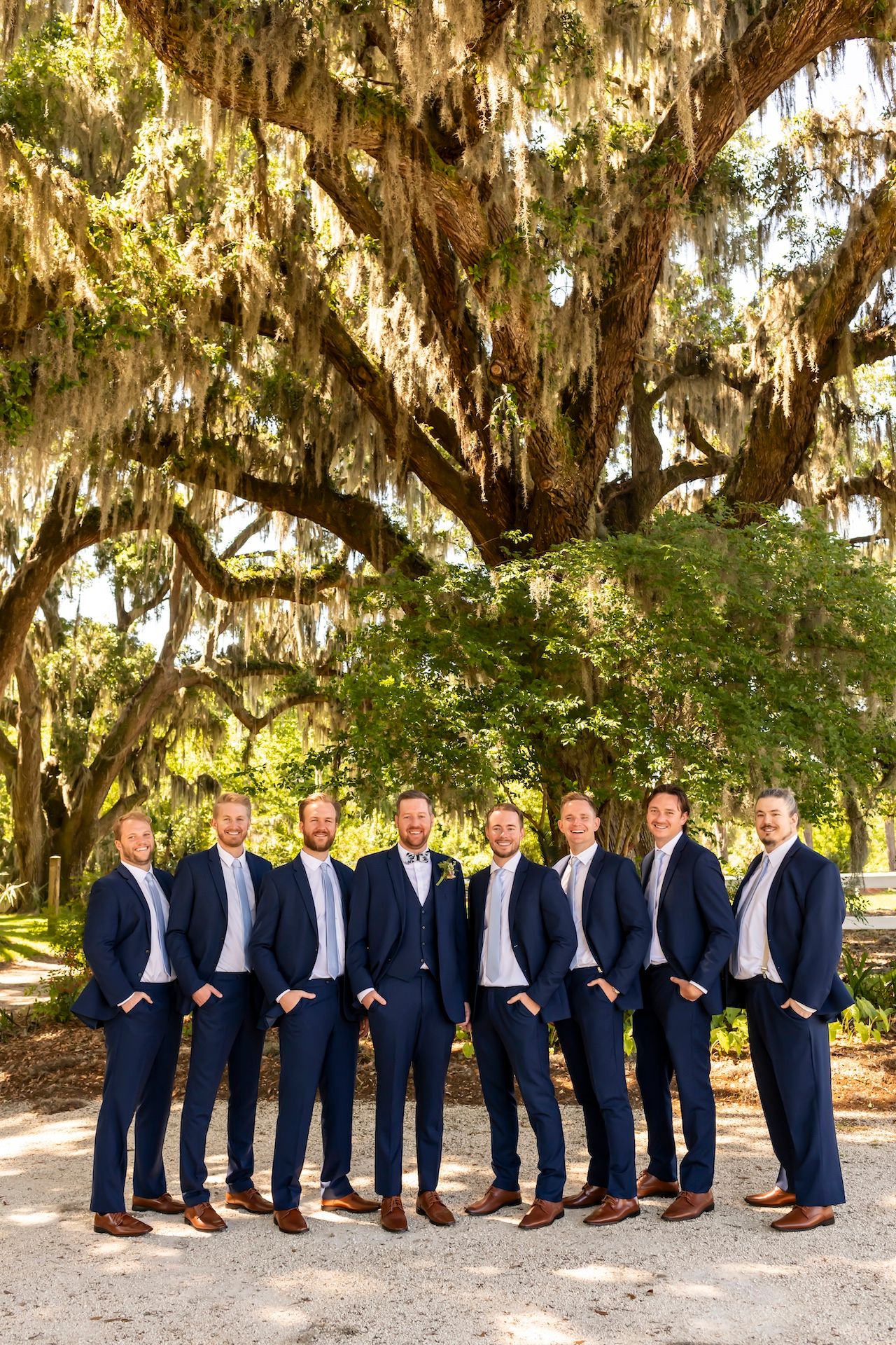 A wedding party in matching navy suits poses beneath a majestic live oak tree draped with Spanish moss.