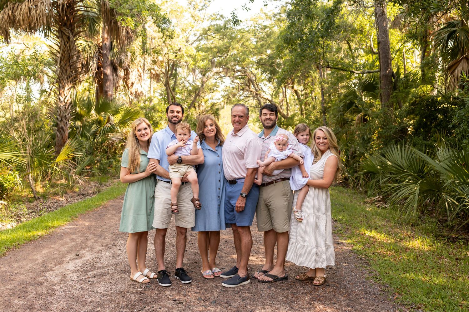 A group stands together on a wooded path during a sunny outdoor photo session in matching neutral colors.