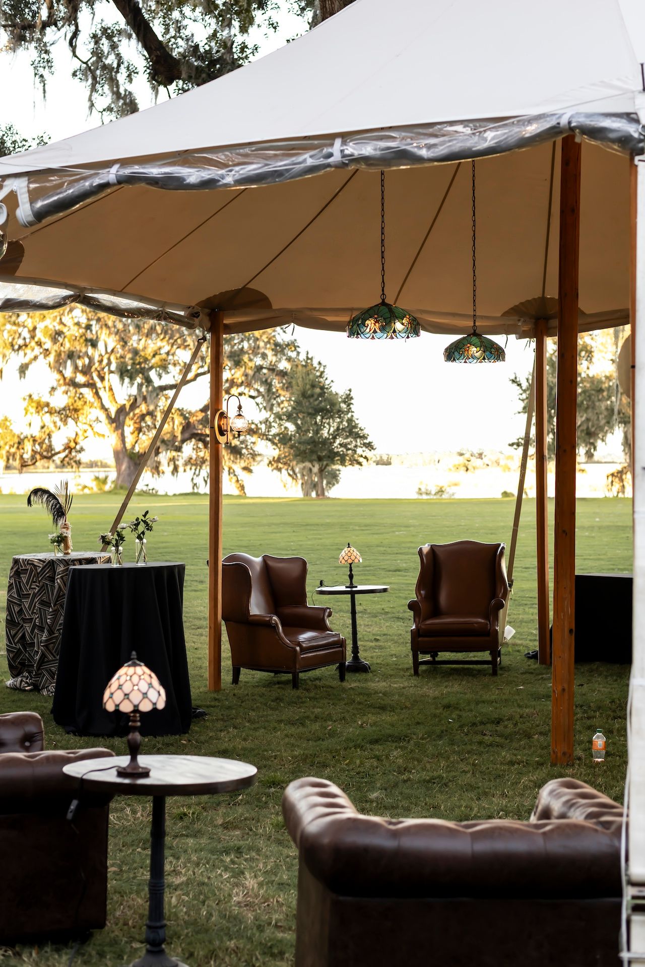 Outdoor lounge area with brown leather chairs under white canopies at sunset on a grassy lawn area.