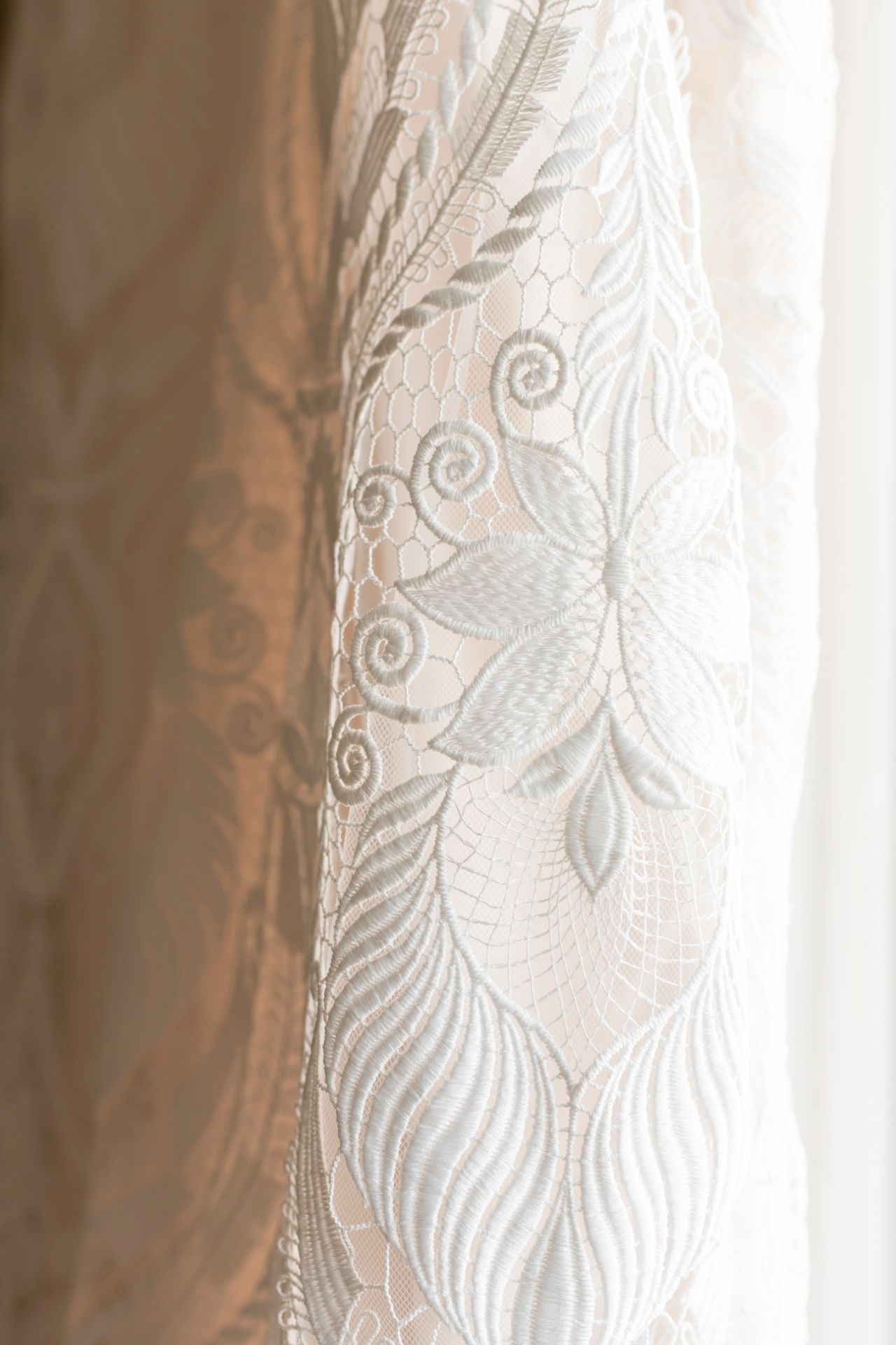 Delicate white lace fabric with intricate floral and swirling patterns featuring elegant embroidered details.